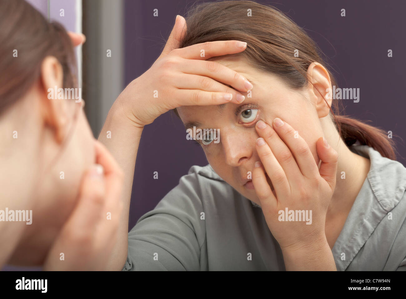 Donna esaminando il suo occhio allo specchio Foto Stock