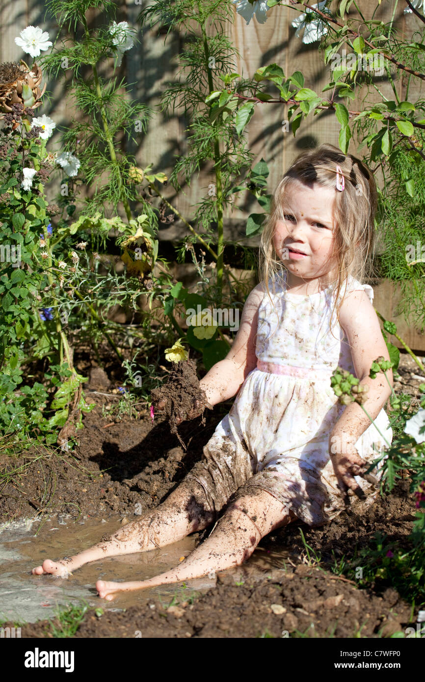Ragazza giovane indossando piuttosto sat nella pozza di fango Foto Stock