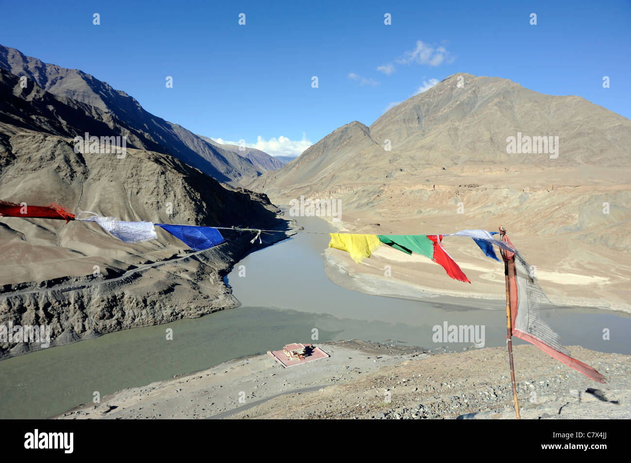 Bandiere di preghiera contrassegnare la confluenza del fiume Zanskar e l'Indus vicino Nimu. Il Indus arriva dalla sinistra. Foto Stock