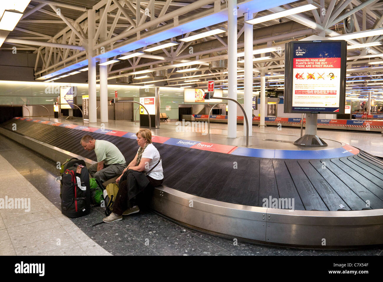 Bagagli smarriti aeroporto; 2 i passeggeri seduti sul bagaglio giostra nella zona di raccolta avente probabilmente perso i loro bagagli, Heathrow airport REGNO UNITO Foto Stock