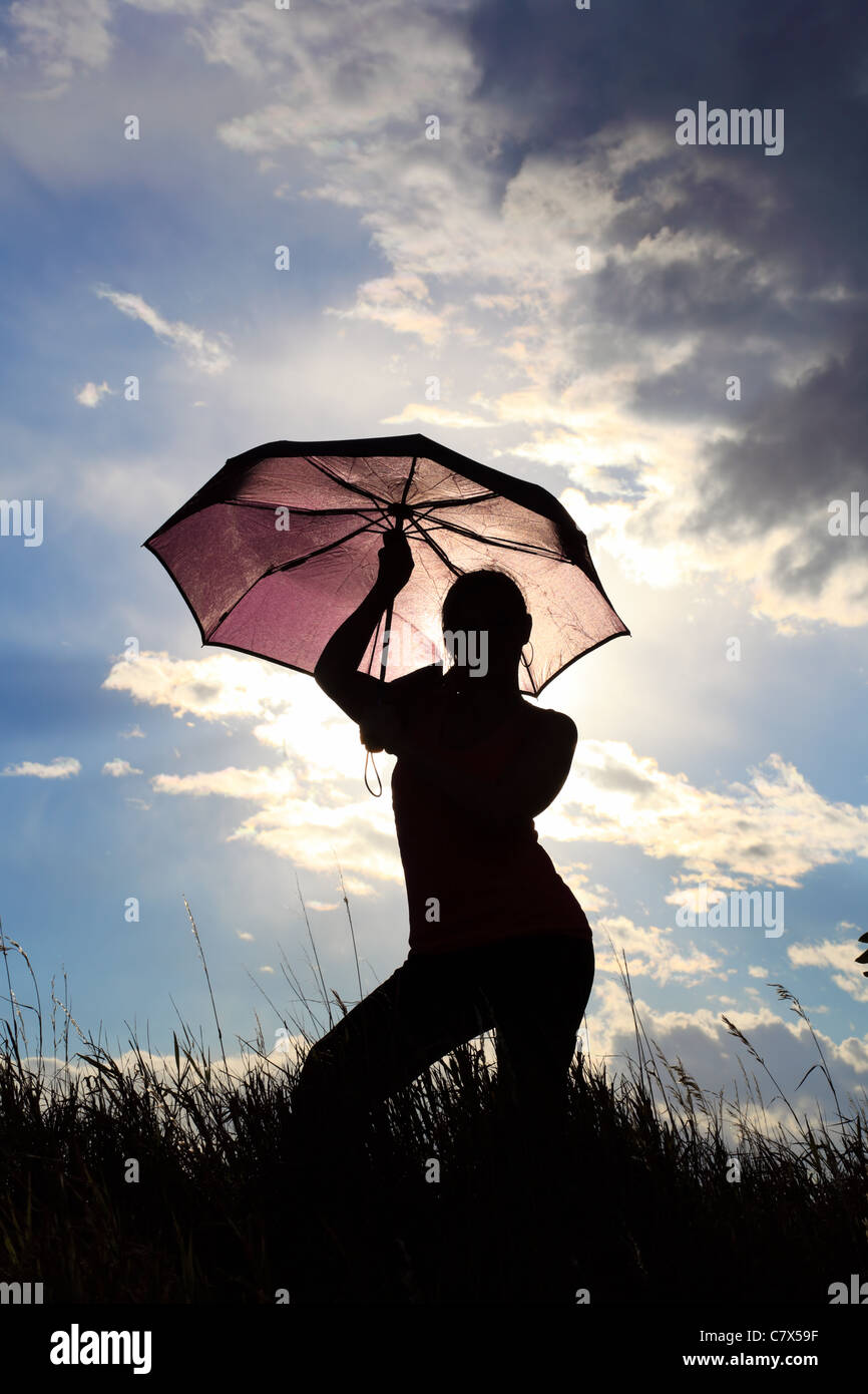 La silhouette di un allungamento ginnasta con un ombrello in un campo Foto Stock