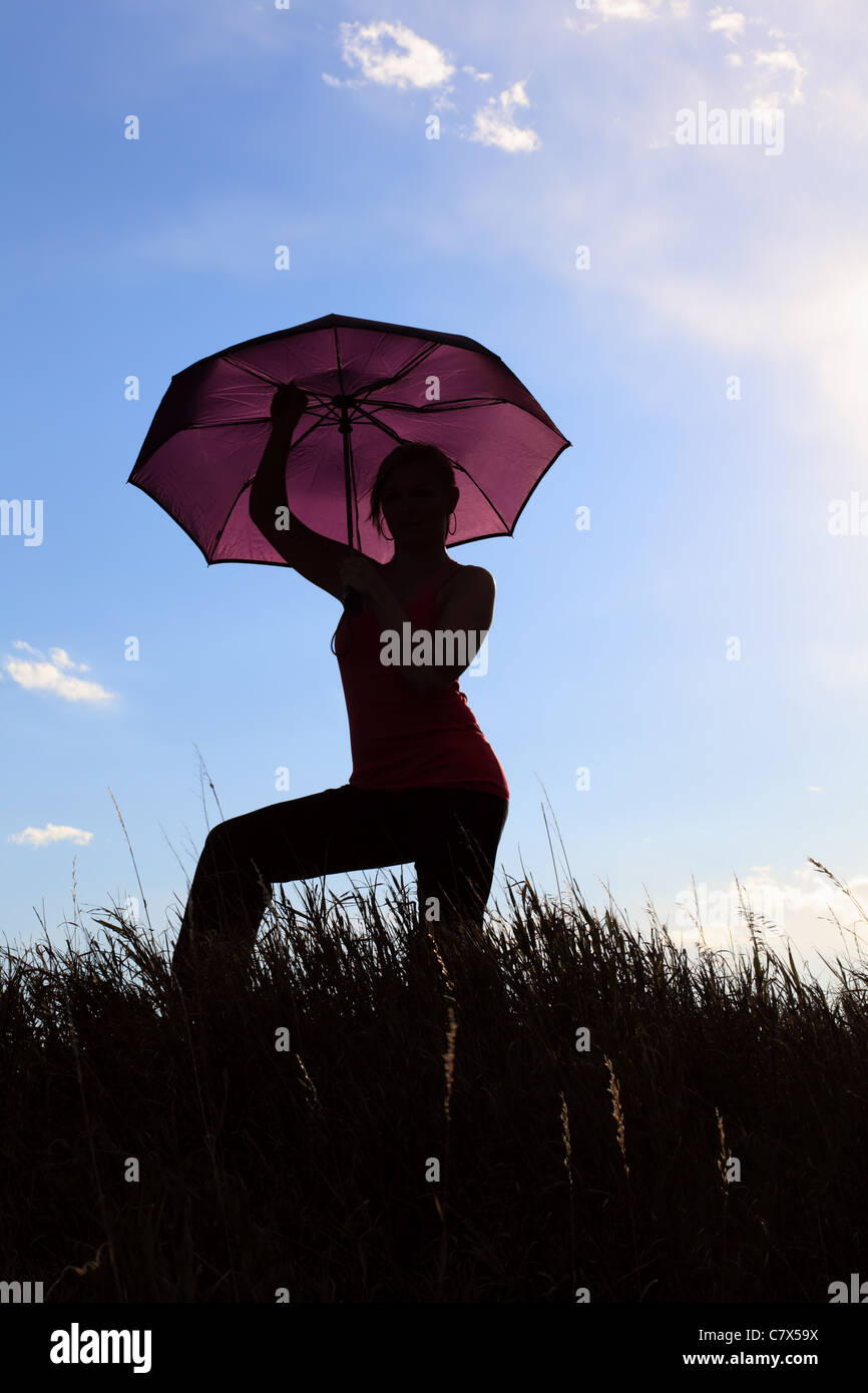 La silhouette di un allungamento ginnasta con un ombrello in un campo Foto Stock