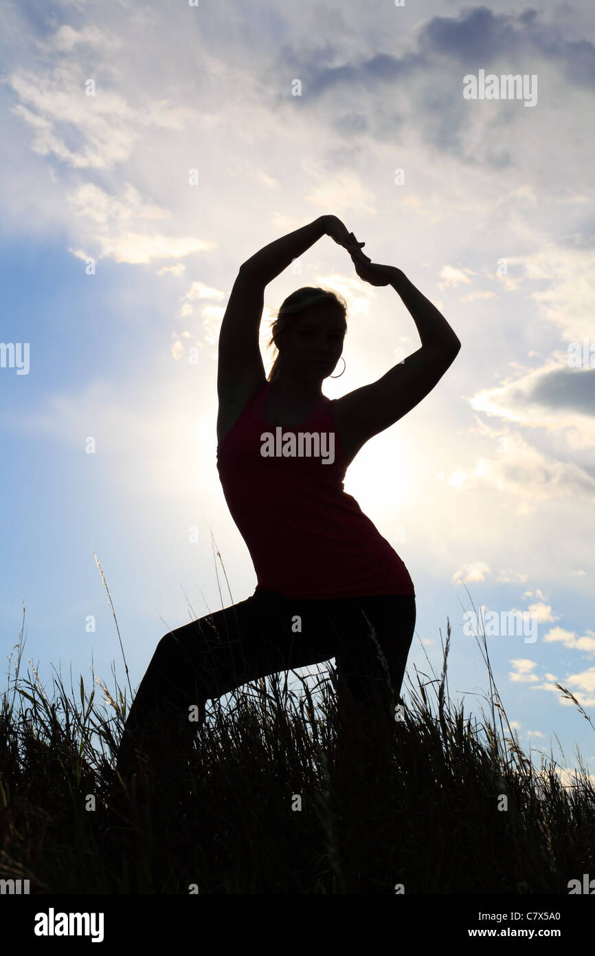 La silhouette di una ginnasta stretching in un campo Foto Stock