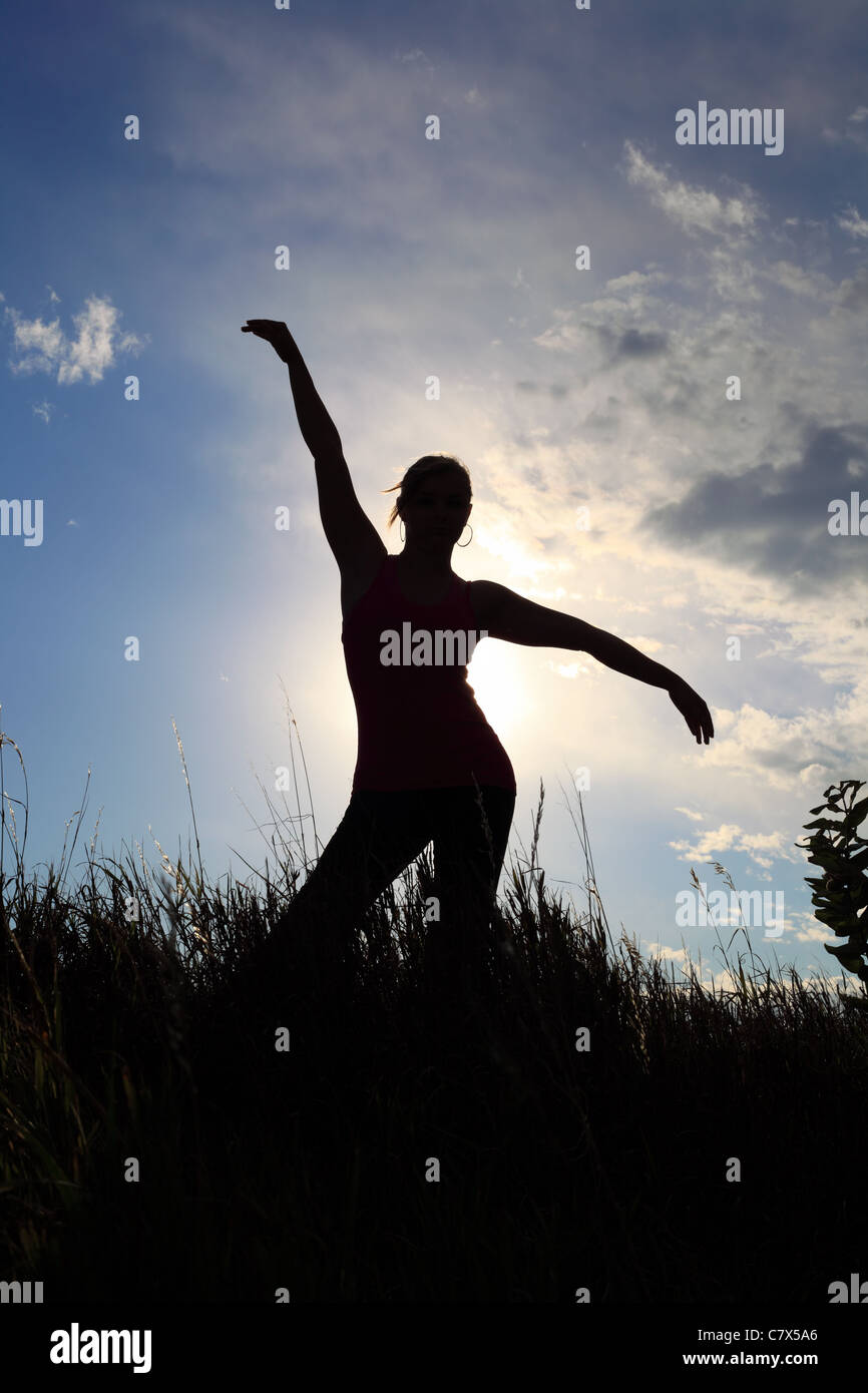 La silhouette di una ginnasta stretching in un campo Foto Stock