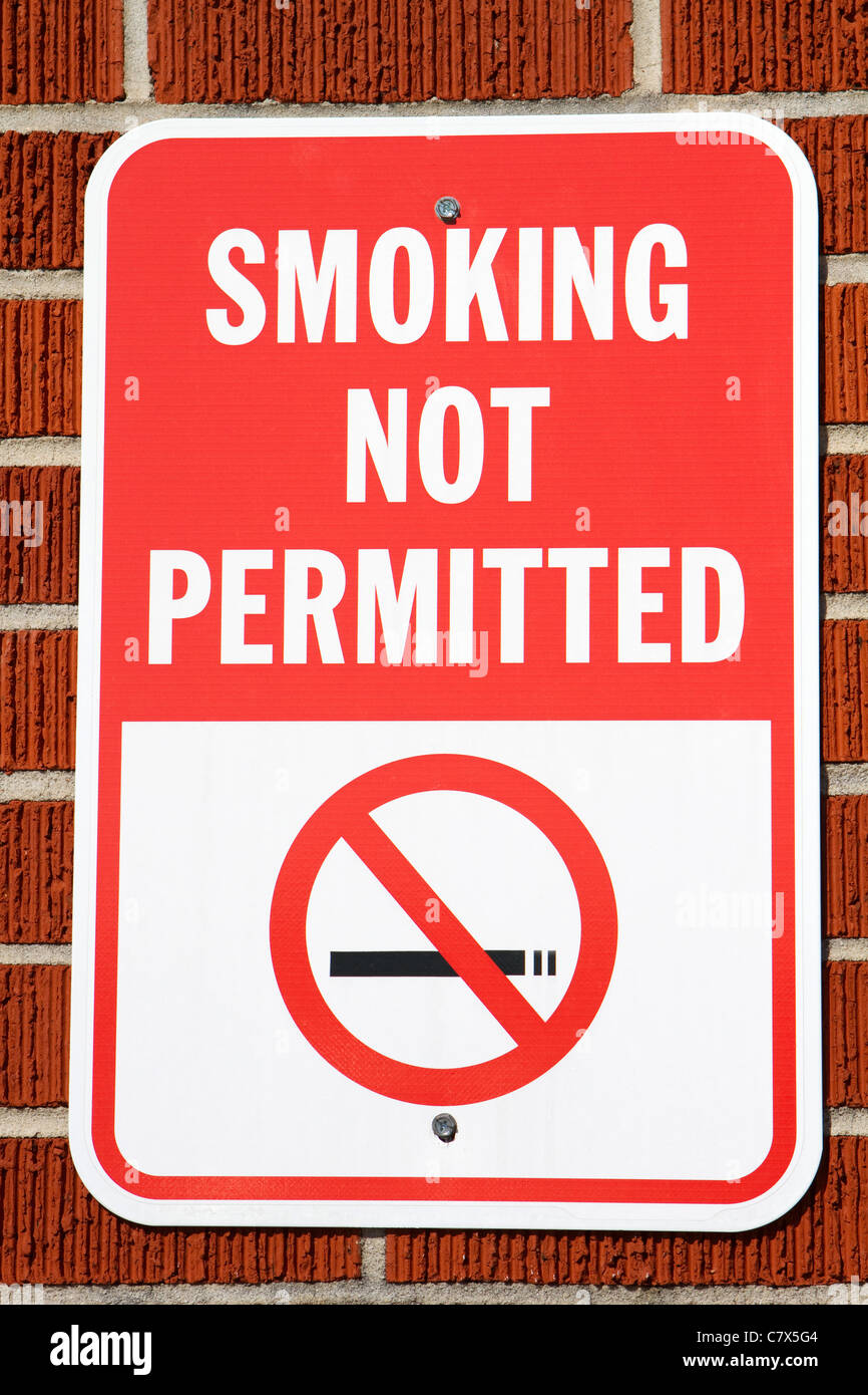 Segno appeso su un muro di mattoni avvertimento che non è consentito fumare nell'area. Foto Stock