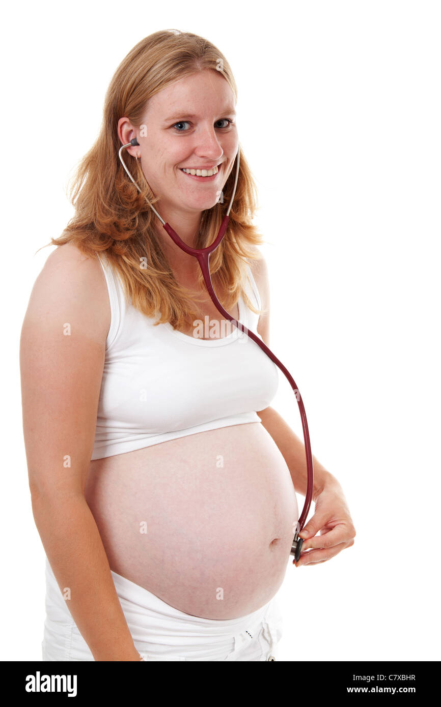 La madre è in ascolto con uno stetoscopio sul ventre in gravidanza su sfondo bianco Foto Stock