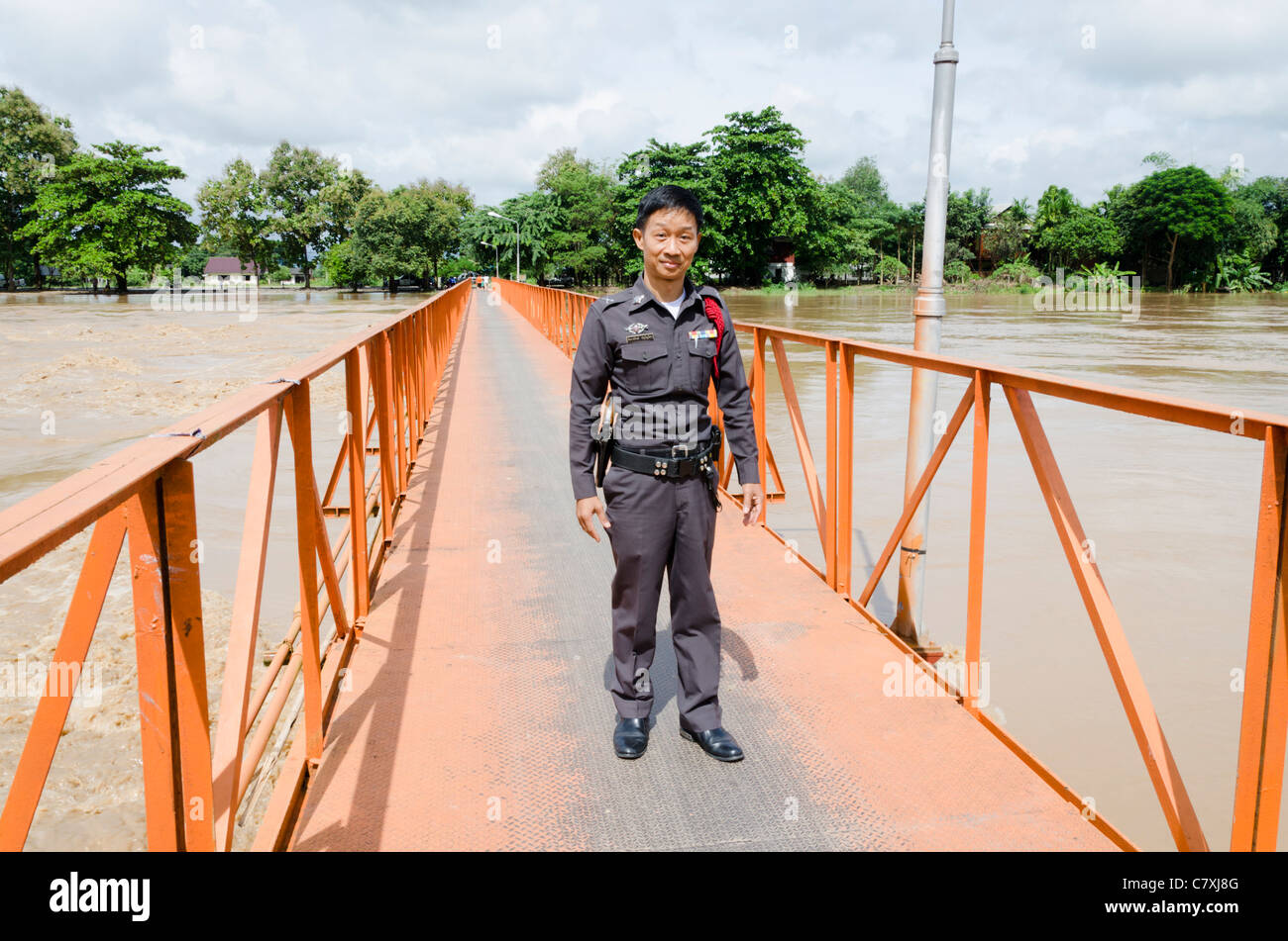 Poliziotto Thai permanente sulla luminosa arancione passerella metallica a allagata Ping diga sul fiume a sud di Chiang Mai nel nord della Thailandia Foto Stock