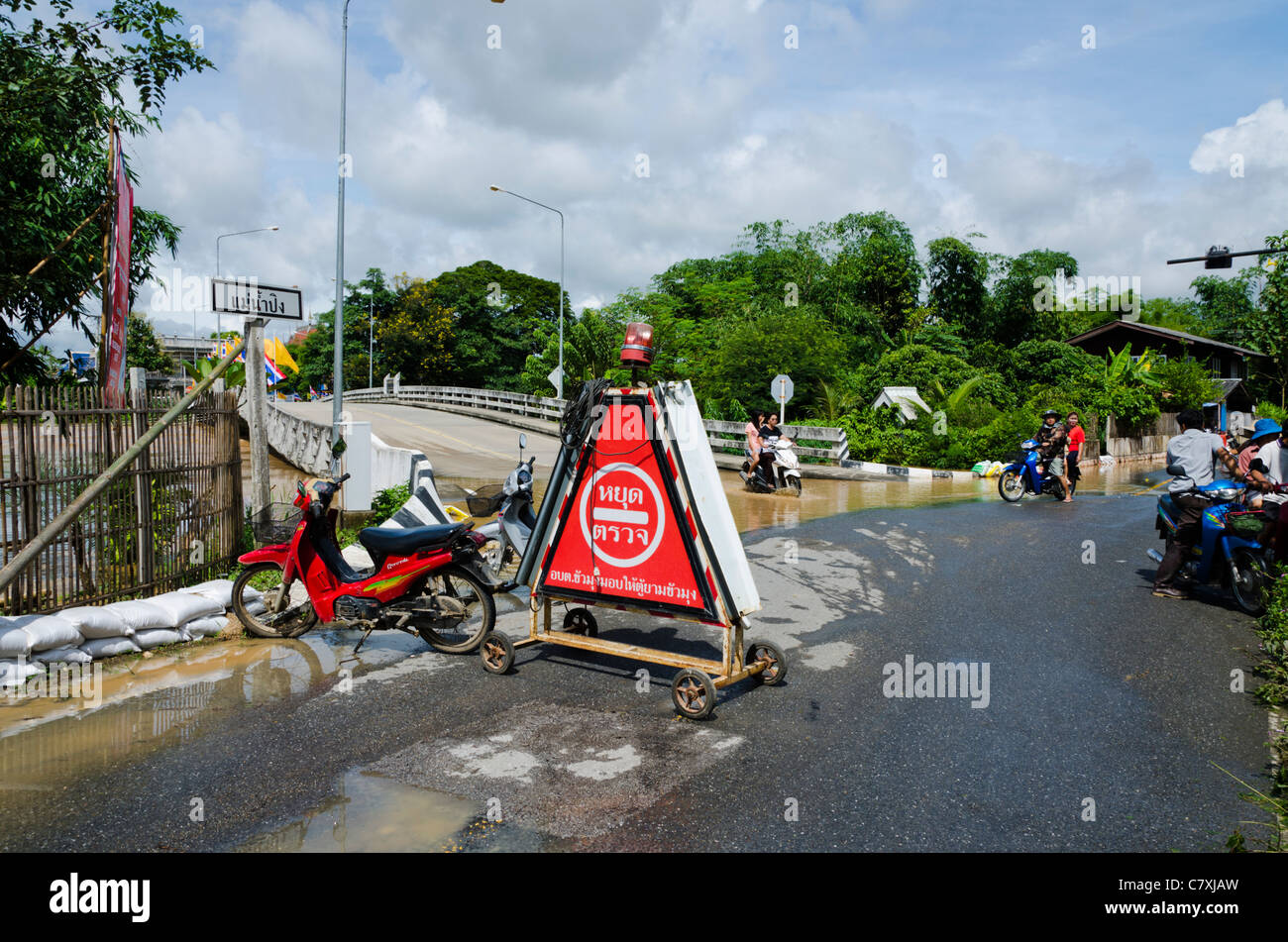 Grande triangolare rosso cartello di avviso in lingua Thai sulla strada a ponte inondato intersezione dal fiume Ping nel nord della Thailandia Foto Stock