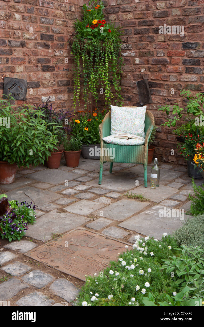 Cortile muro mattoni giardino recintato con pietra rigenerata pavimentazione lastre patio pavimentato - poltrona sedia ed erbe e fiori in pentole di terracotta vecchia UK Foto Stock