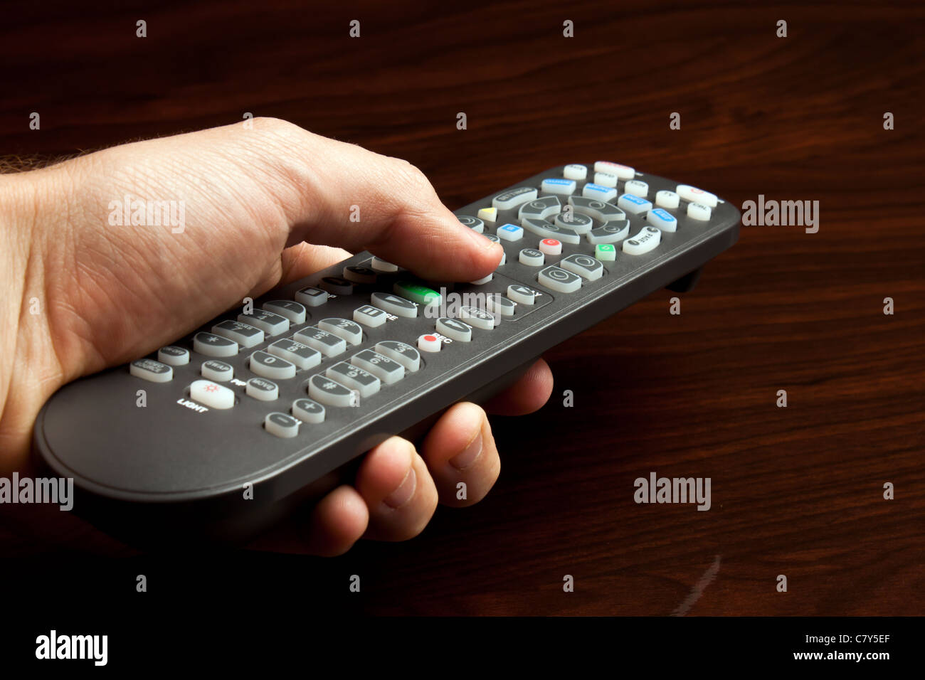 La mano di puntamento remoto televisione contro la superficie di legno Foto Stock