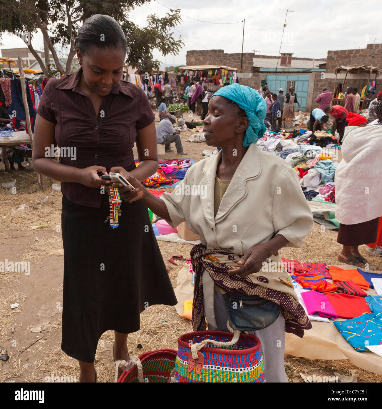 Due donne africane completare una transazione di mercato utilizzando M-PESA, un telefono cellulare basato il servizio Trasferimento di denaro Foto Stock