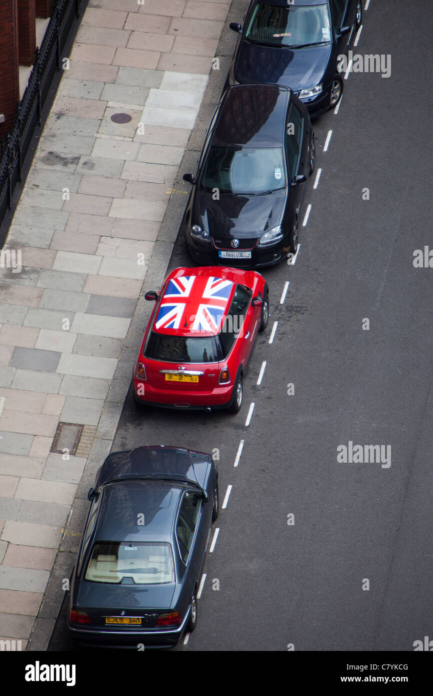 Un rosso brillante Mini auto con un raccordo martinetto tetto si distingue da altre macchine parcheggiate su una strada residenziale a Londra Foto Stock