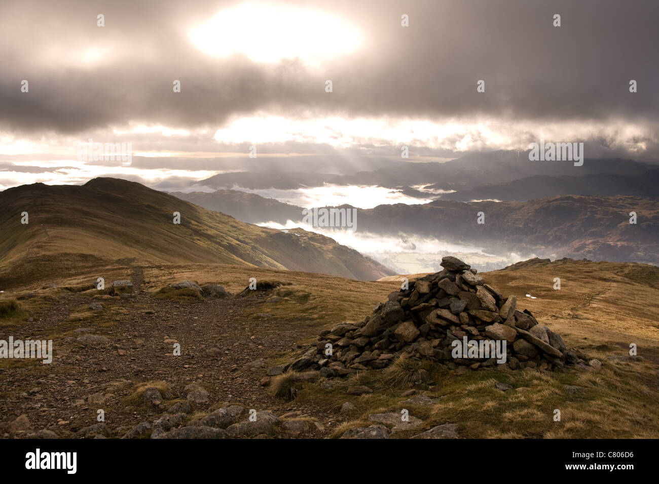 Un lone cairn sul vertice del Fairfield Horseshoe Ridge e flussi di luce solare attraverso la nebbia copriva valley Foto Stock