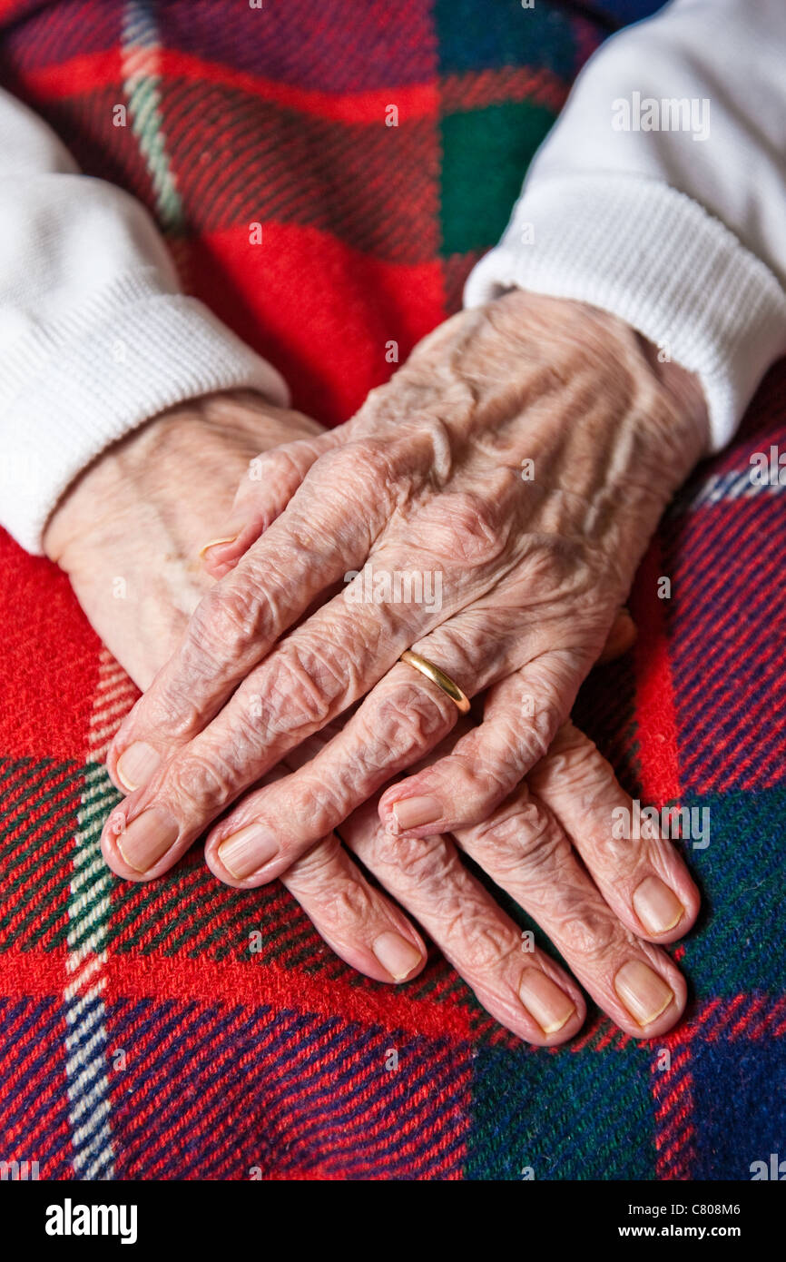 Le mani di ottanta nove anni di grande nonna in appoggio su una coperta di tartan Foto Stock