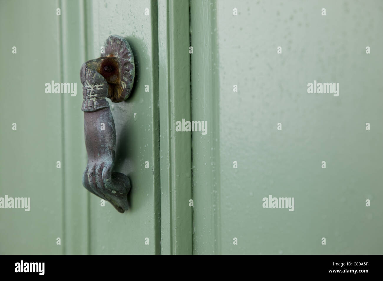 L'immagine orizzontale di una porta respingente in la forma di una mano si blocca su un panno verde porta di legno sotto la pioggia. Foto Stock