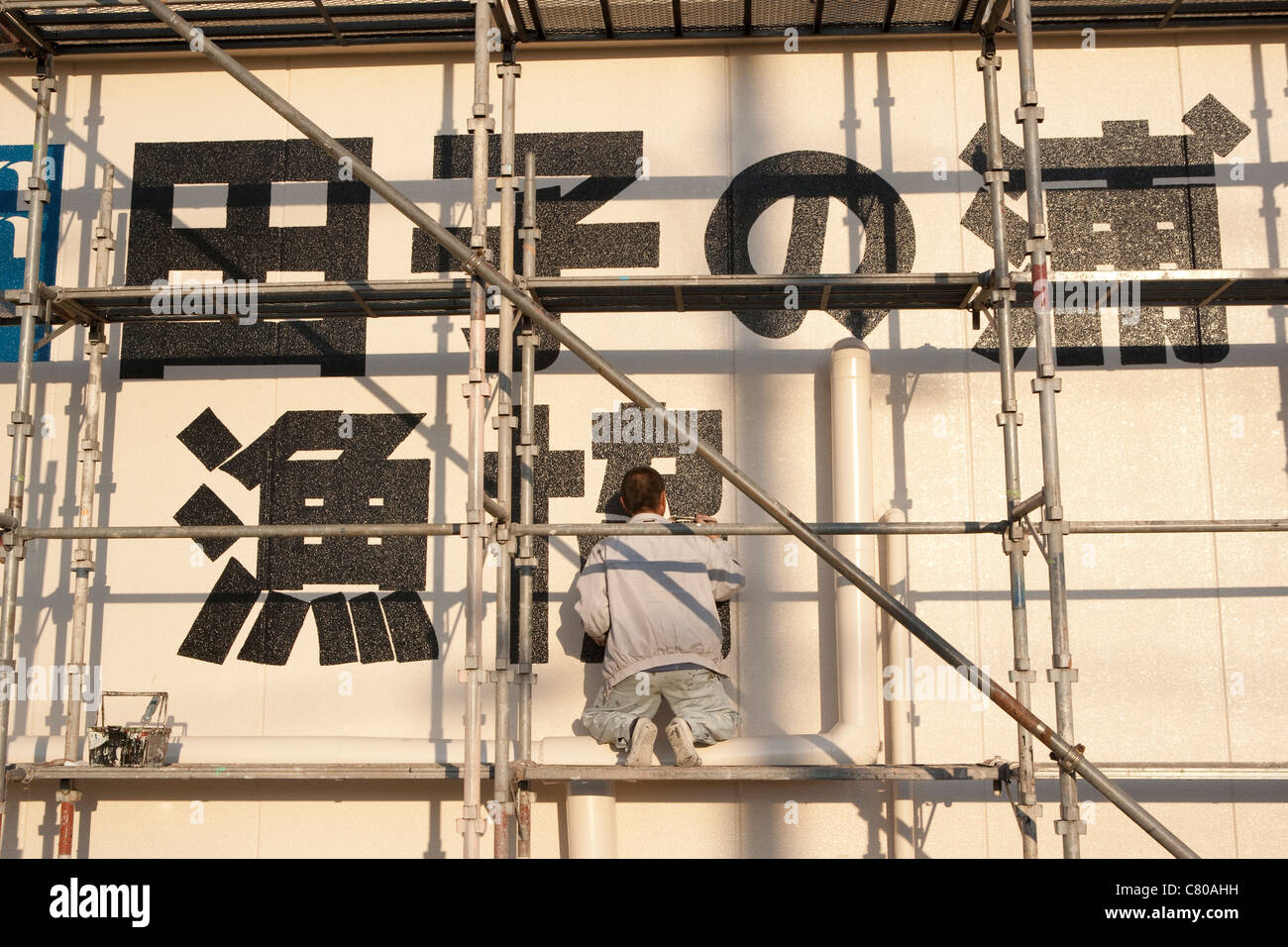 Uomo su scarffold paintng segno sulla costruzione, Giappone Foto Stock