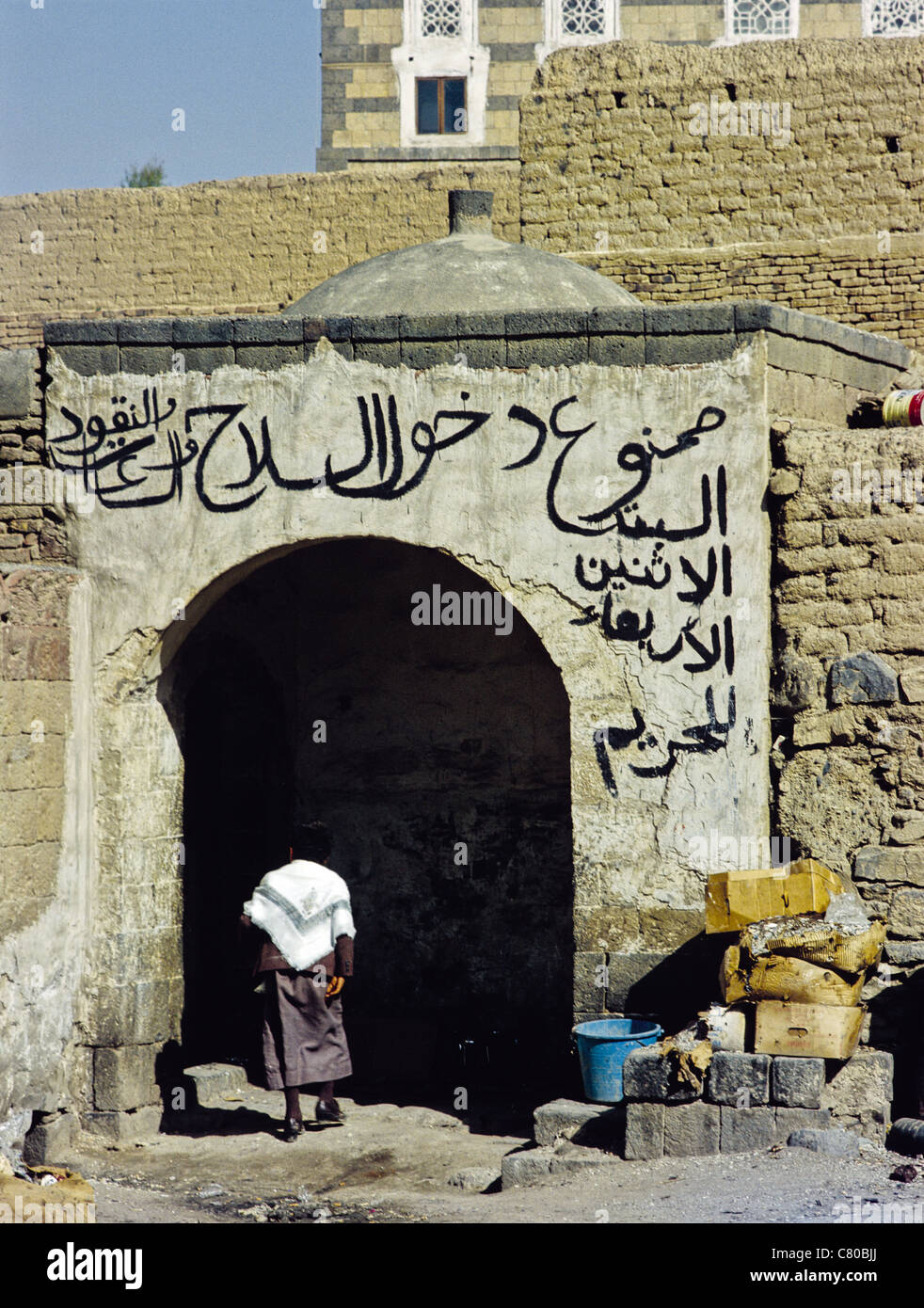 Bambino di entrare in un edificio con la calligrafia Araba al di sopra della porta nella città vecchia di Sana'a, Yemen Foto Stock