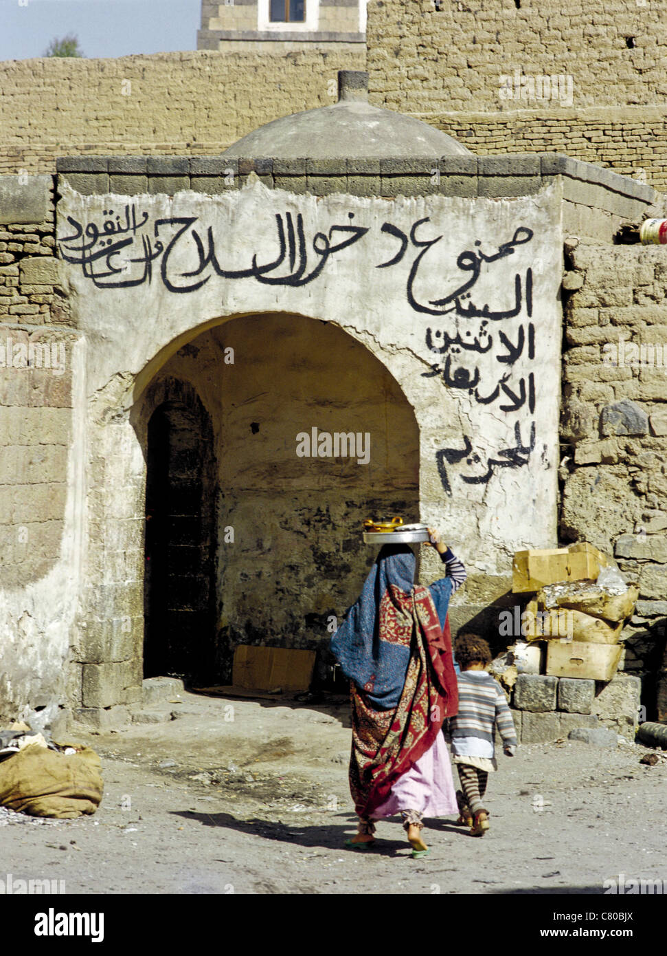 Donna yemenita e bambino di entrare in un edificio con scrittura araba al di sopra della porta nella città vecchia di Sana'a, Yemen Foto Stock