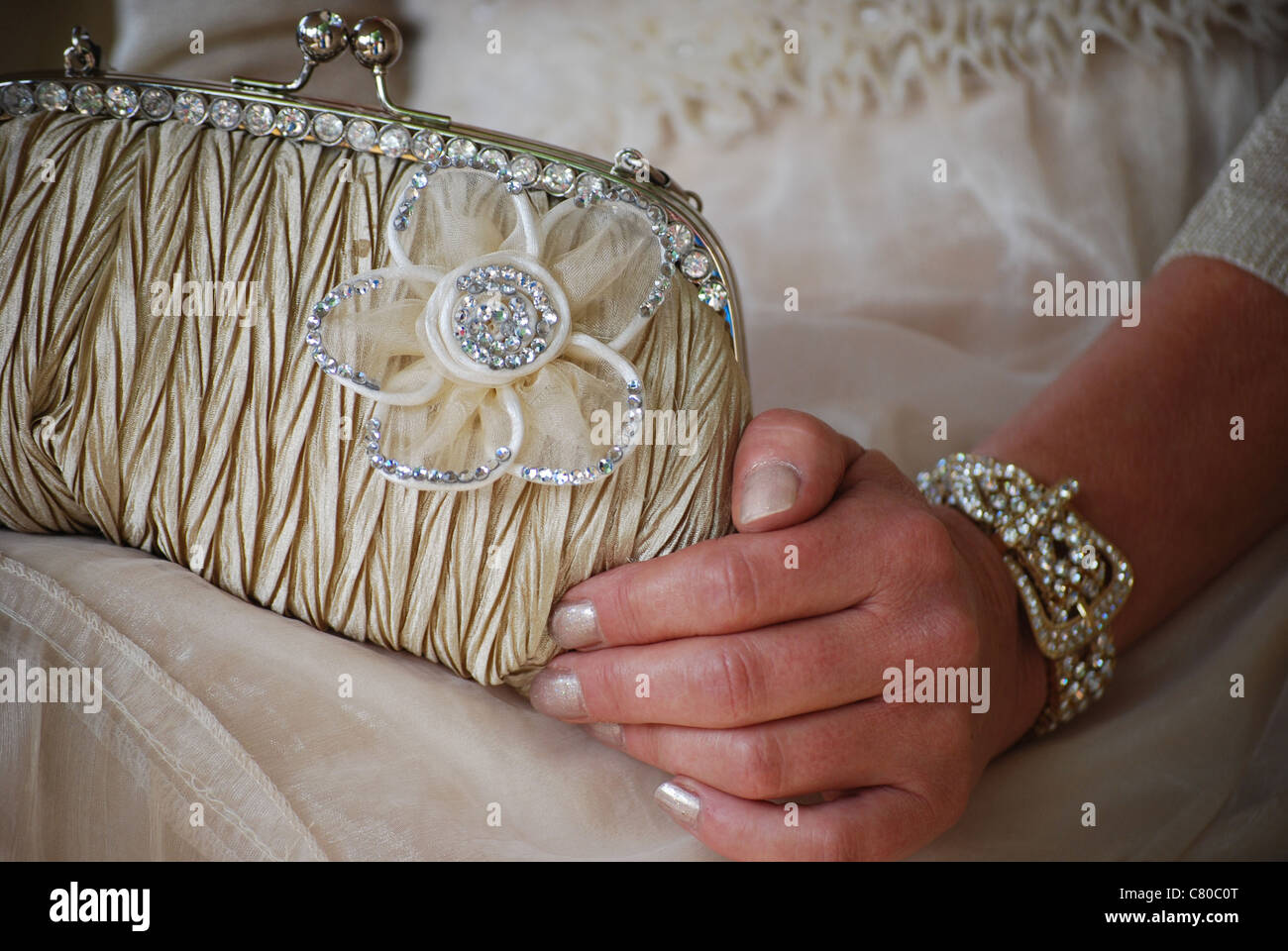 Una sposa che indossa un braccialetto di diamante, tenendo in mano un sacchetto in raso con fiore dettaglio. Foto Stock