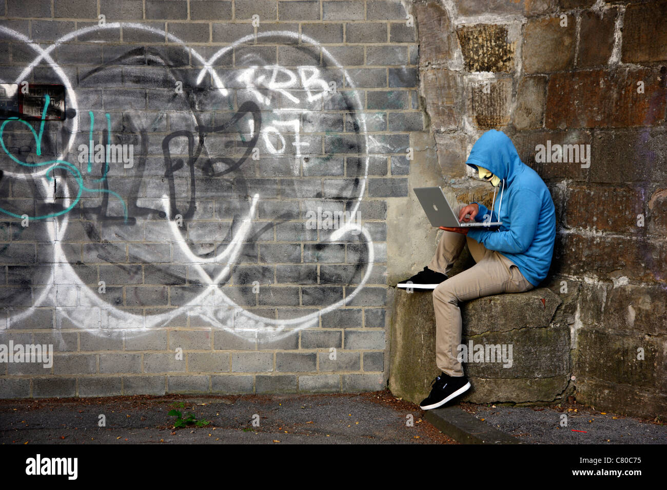 Il computer utente, hacker, siede conspiratorially con un portatile, di fronte a un graffiti. Immagine di simbolo, computer-la criminalità su Internet. Foto Stock