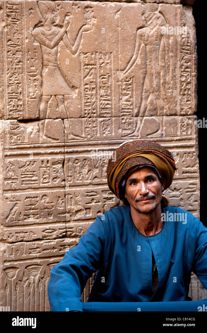 Egyptian uomo seduto di fronte al Tempio di Horus di geroglifici. Edfu, Egitto Foto Stock