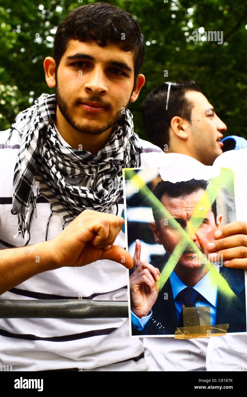 Uno protester pone con un cassonetto con le foto di Bashar al-Assad. Foto Stock