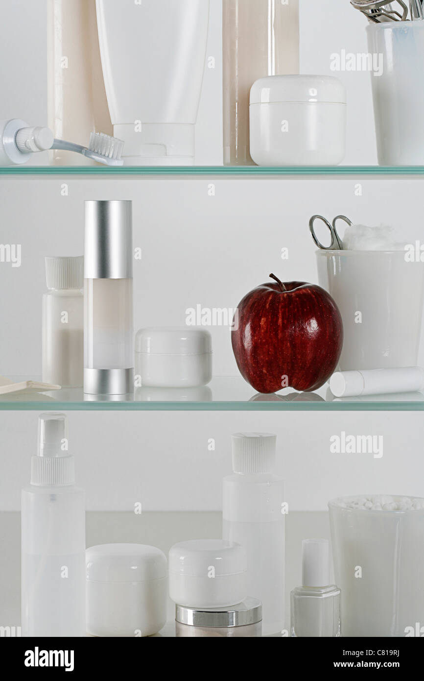 Armadietto pieno di dermocosmesi prodotti e una mela rossa Foto Stock