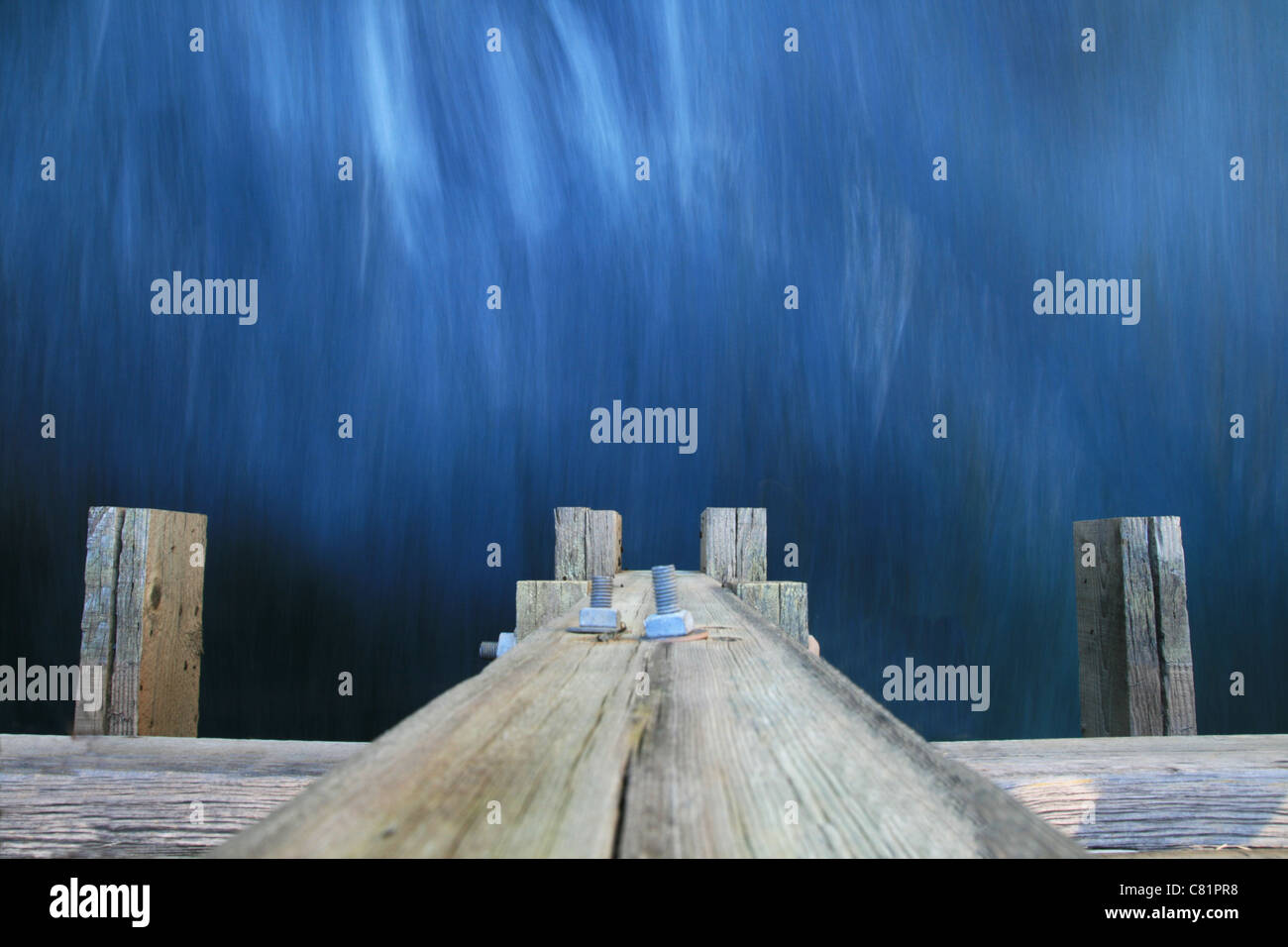 Una lunga esposizione di acqua che scorre sotto un ponte di legno con movimento acqua sfocata Foto Stock