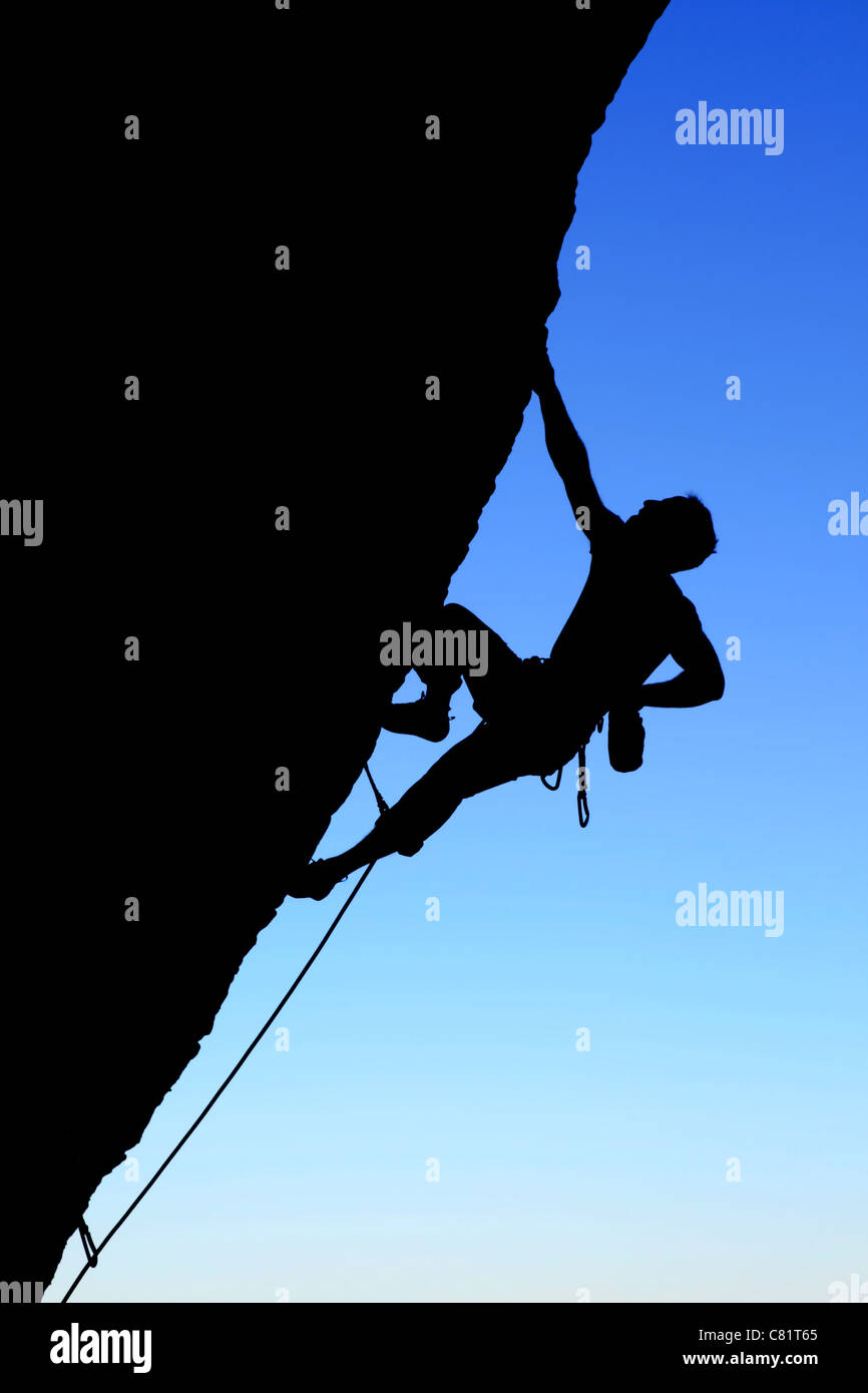 Silhouette di rocciatore salendo una rupe a strapiombo con cielo blu sullo sfondo Foto Stock