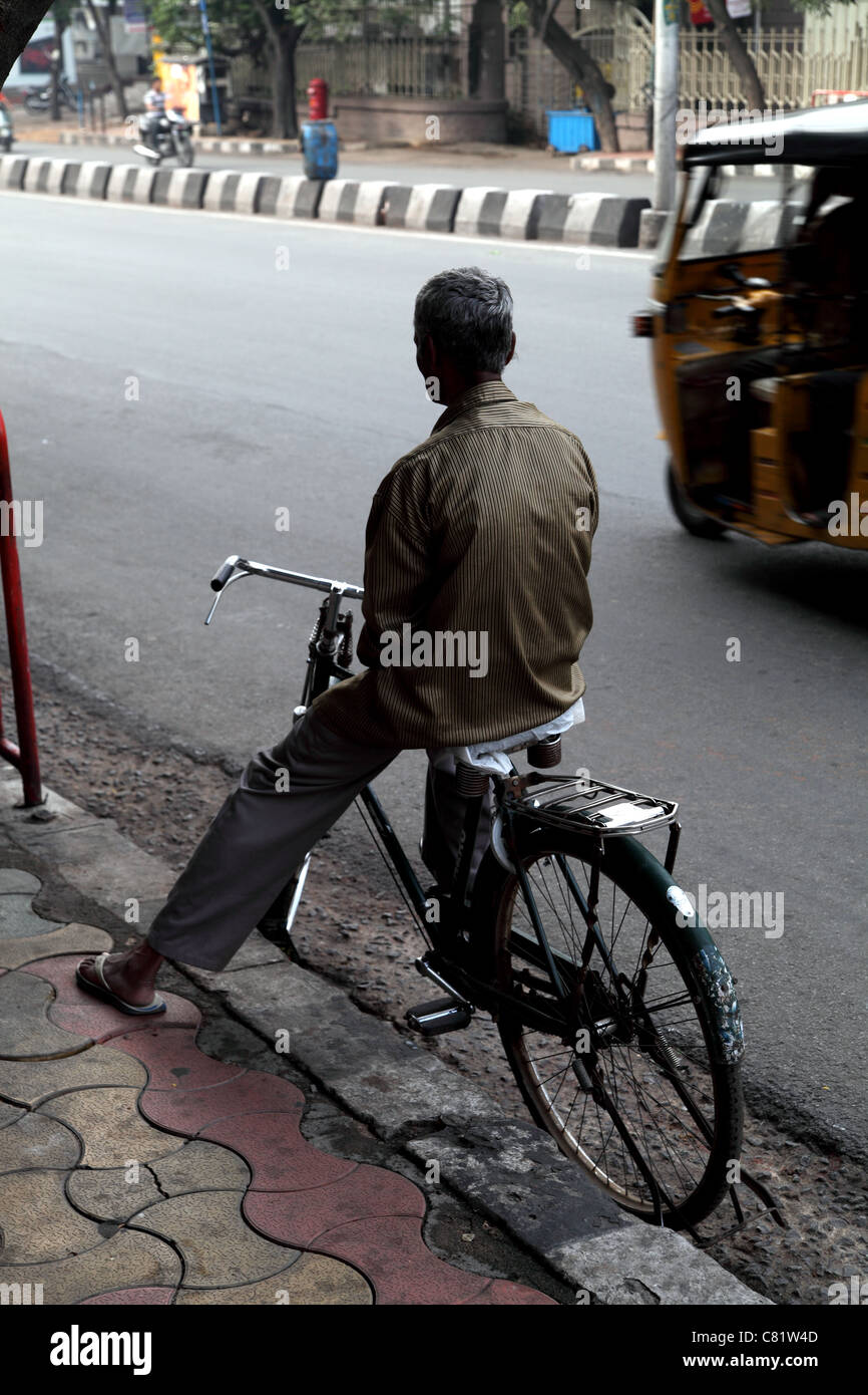 Vista posteriore del uomo indiano in attesa di bicicletta da strada come un autorickshaw passa Foto Stock