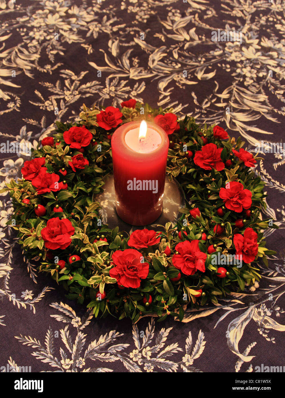 Rosso illuminato candela circondato da rosso e verde di decorazione su un piano di un tavolo Foto Stock