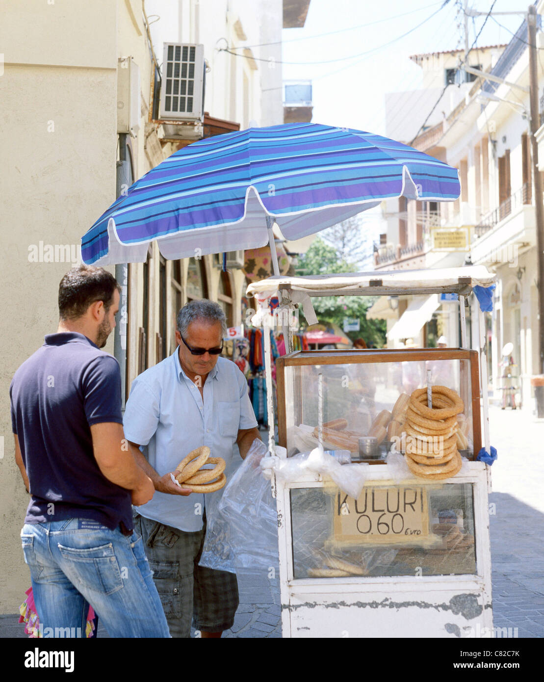 Un venditore ambulante in Rethymnon, Creta, vende koulouri - semi di sesamo incrostati di pane cerchi - per un cliente. Foto Stock