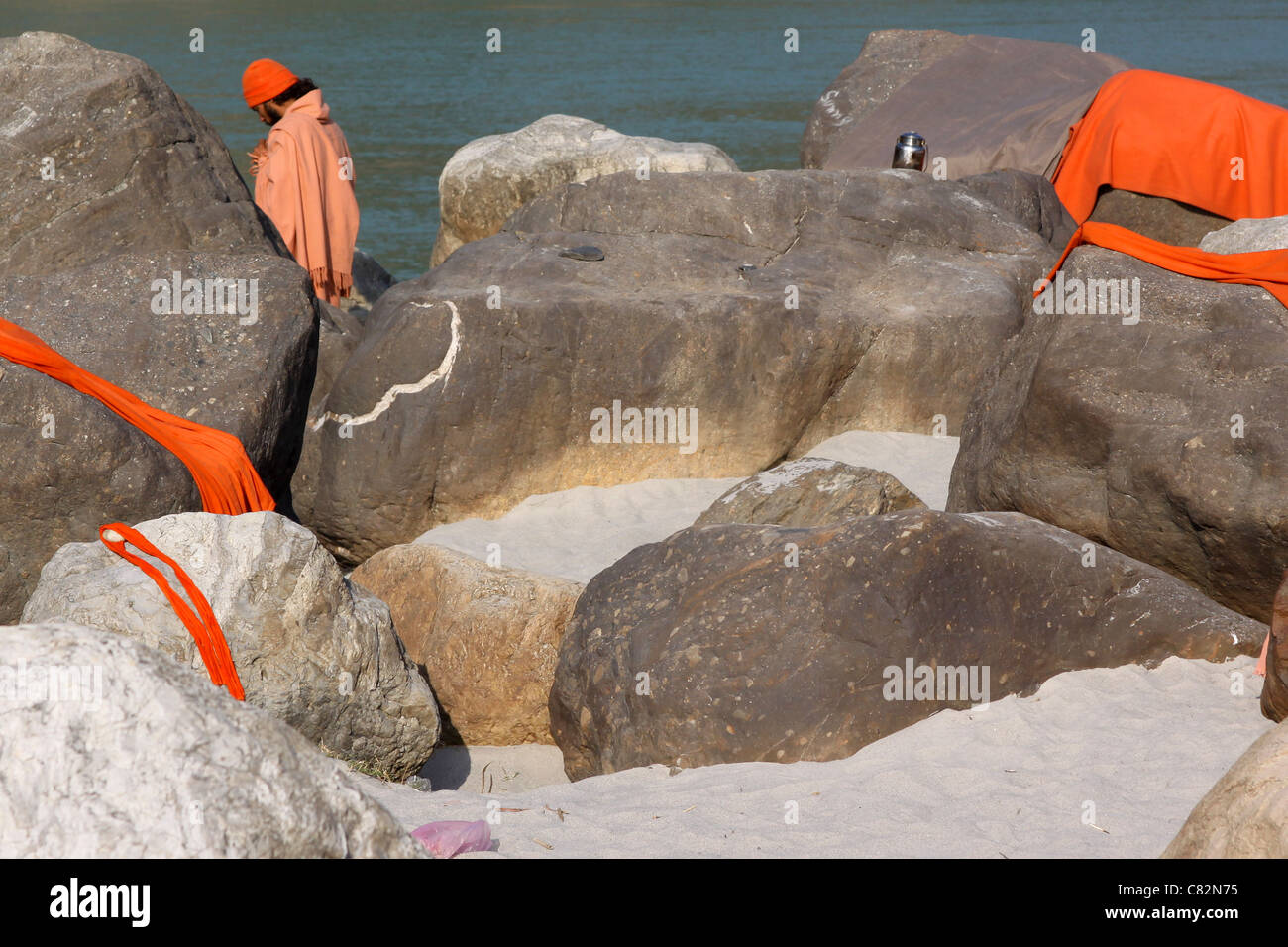 Pregando sadhu tra le rocce con i coperchi di colore arancione su una banca del fiume Gange Foto Stock