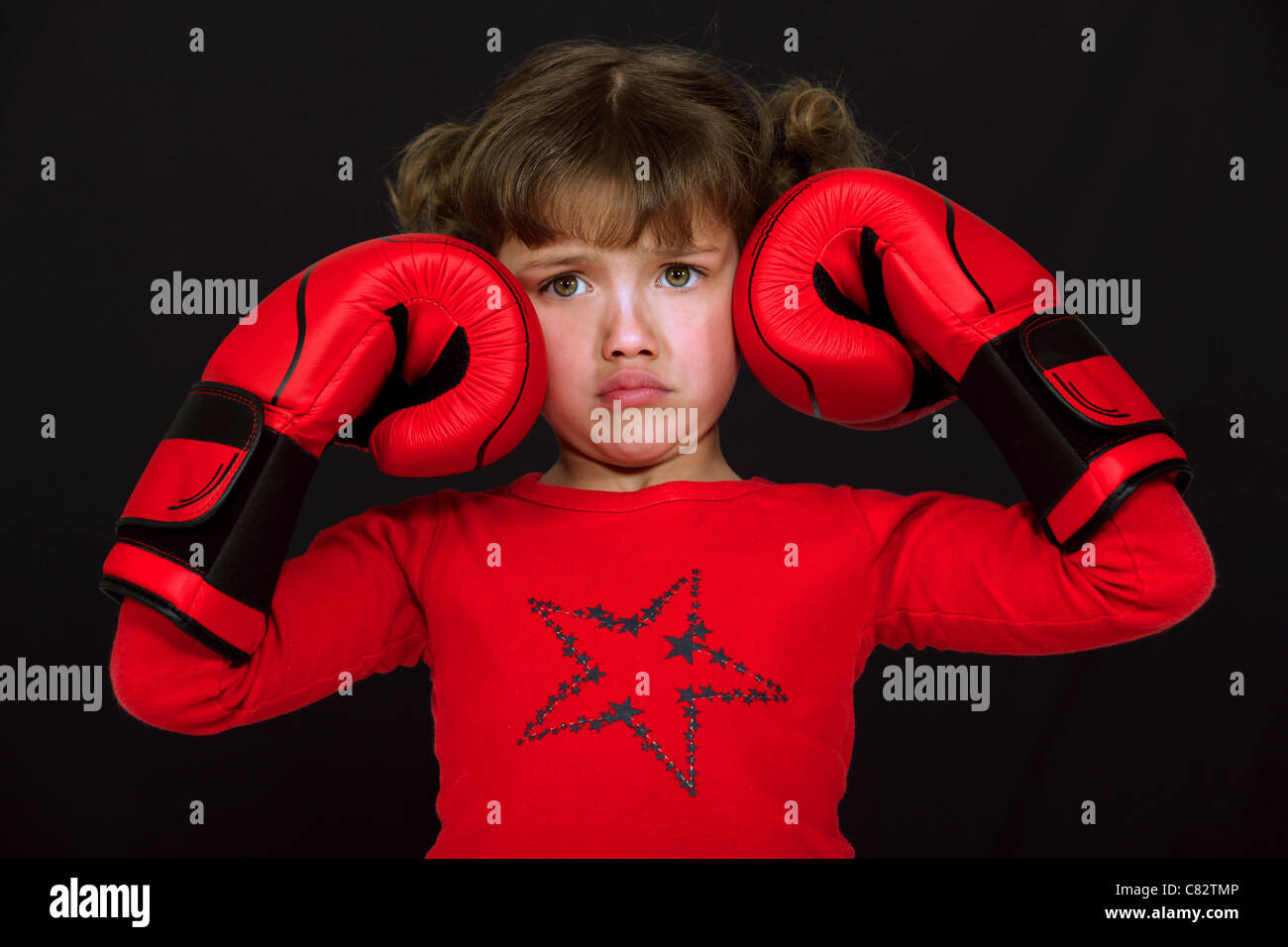 Bambina con i guantoni tirando una faccia su sfondo nero Foto Stock