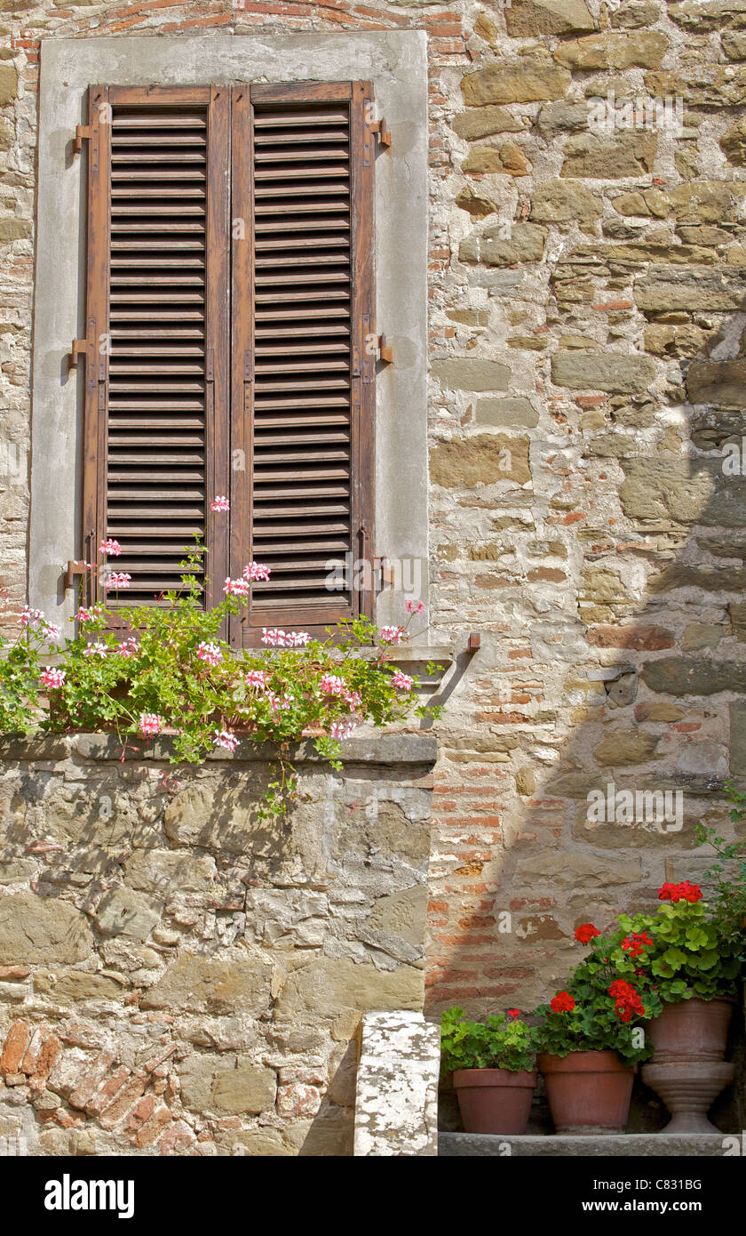 Legno marrone persiane alle finestre con fiori in un borgo medievale in Toscana Foto Stock