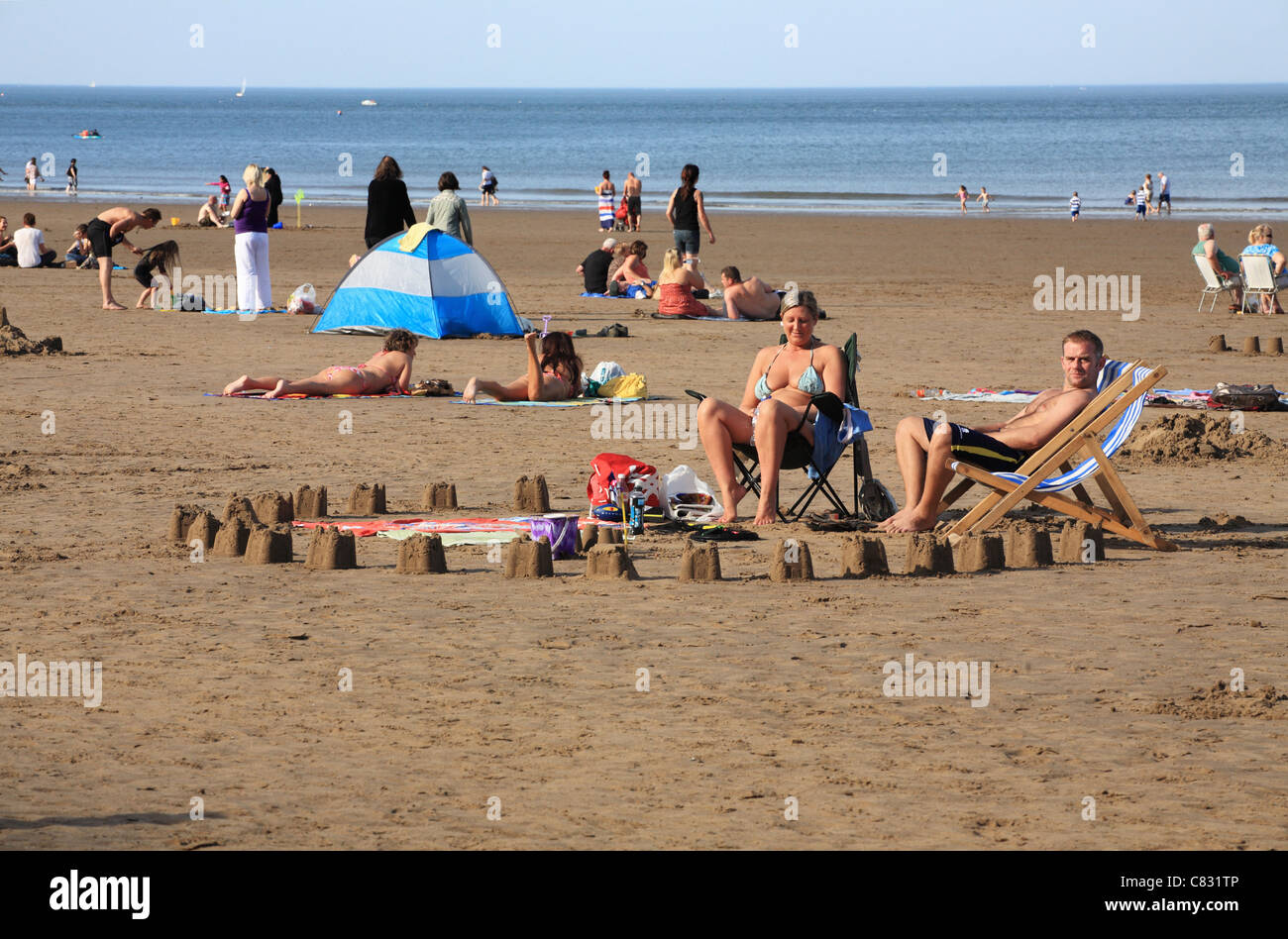 Giovane seduti su sedie a sdraio e circondata da castelli di sabbia sulla spiaggia di Whitby Foto Stock