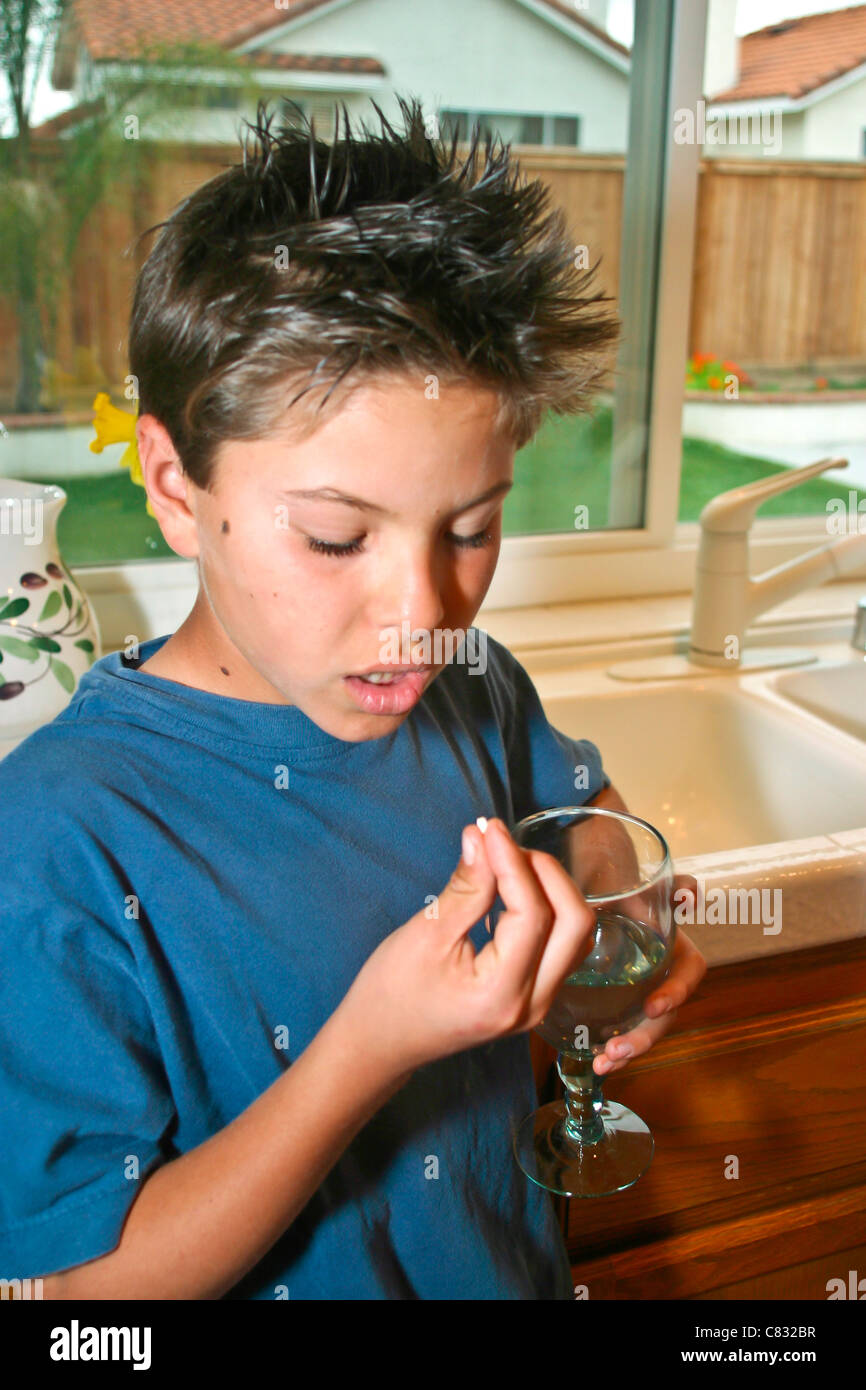 Giapponese/Caucasian 9-10 anno vecchio ragazzo prende la pillola con un bicchiere di acqua. Signor © Myrleen Pearson Foto Stock