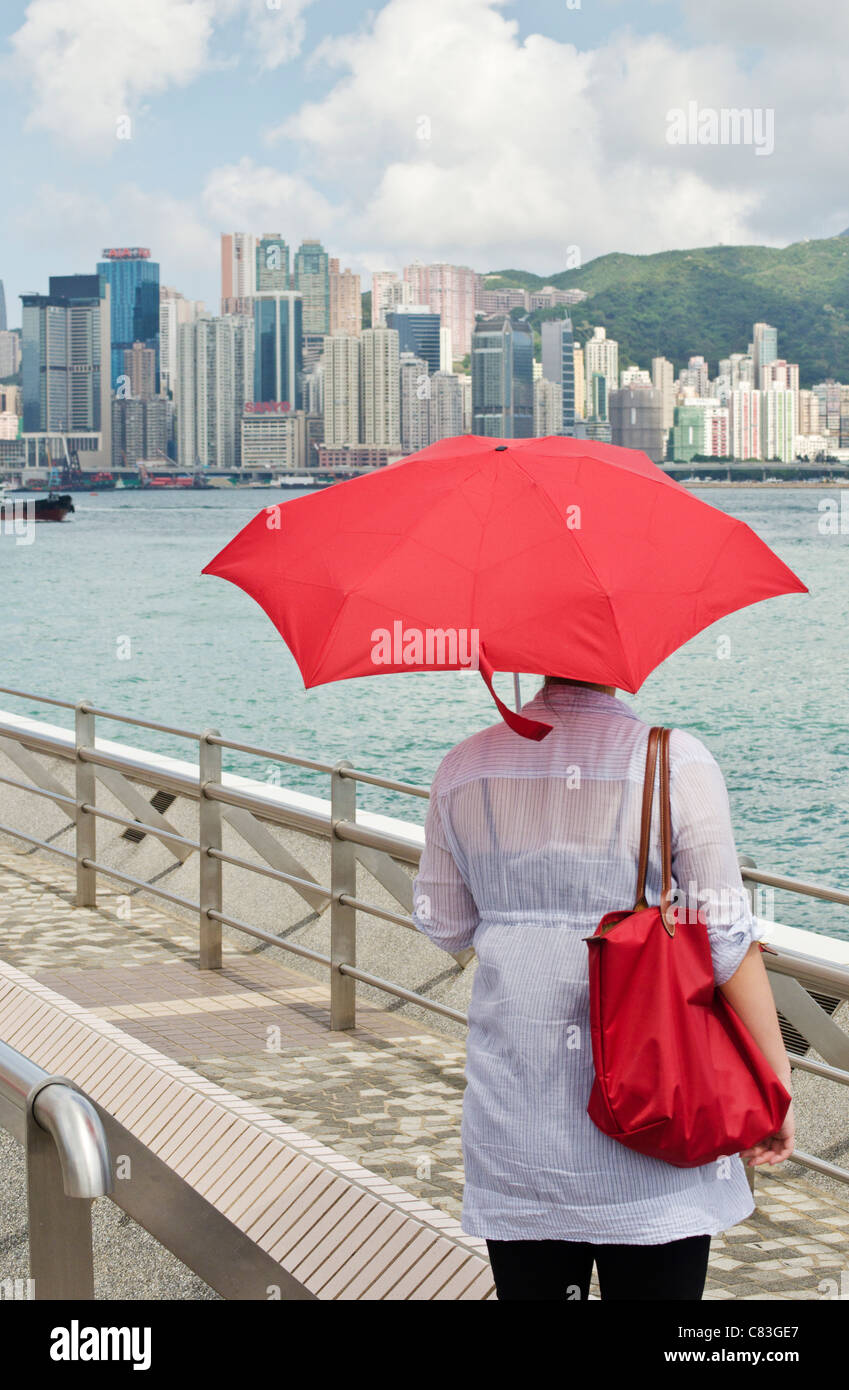 Donna con ombrello rosso guardando sopra la baia di Victoria in Hong Kong Foto Stock