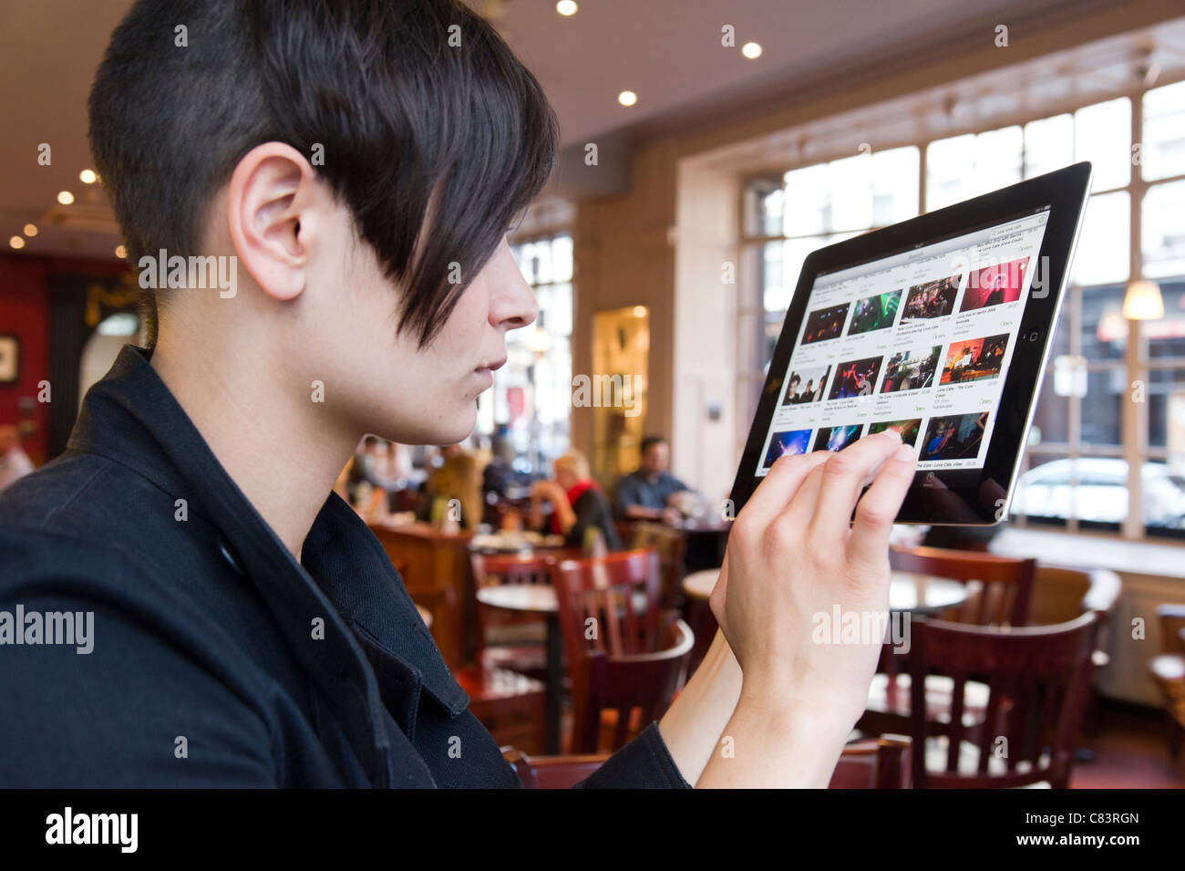 Giovane donna navigando i video di YouTube su un iPad di Apple Computer tablet utilizzando coffee shop gratuito wi fi, London, England, Regno Unito Foto Stock