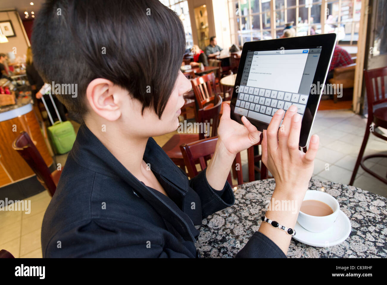 Giovane donna l'invio di messaggi di posta elettronica su un iPad di Apple Computer tablet utilizzando coffee shop gratuito wi fi, London, England, Regno Unito Foto Stock