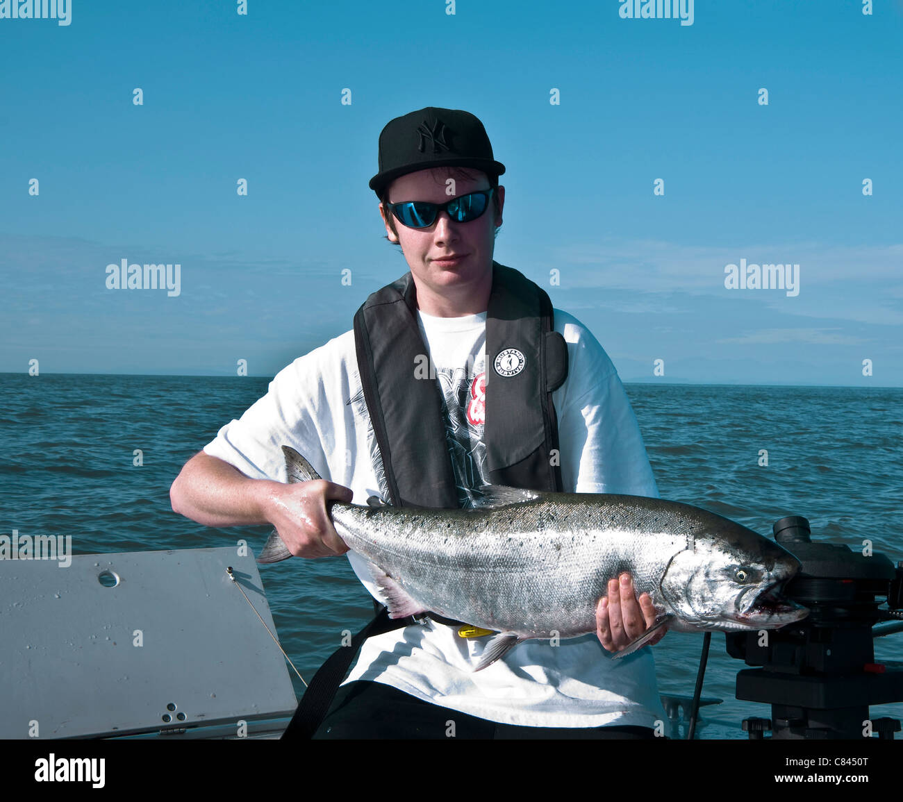 Ragazzo che indossa un New York baseball hat personale e dispositivo di galleggiamento con una molla il salmone pescato nel porto di Vancouver Foto Stock