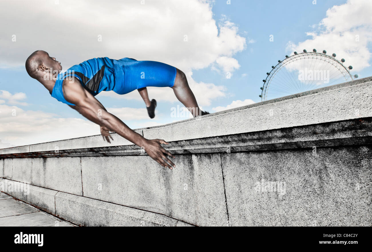 Vaulting atleta oltre il muro di pietra Foto Stock
