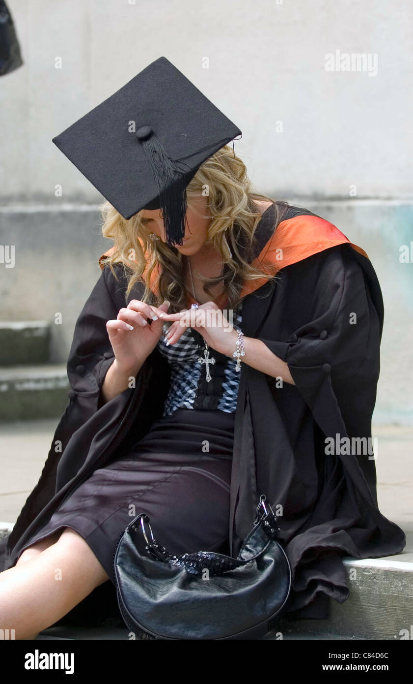 Annoiato Swansea University Graduate femmina in attesa per la cerimonia per iniziare a Brangwyn Hall a Swansea, Galles del Sud. Foto Stock