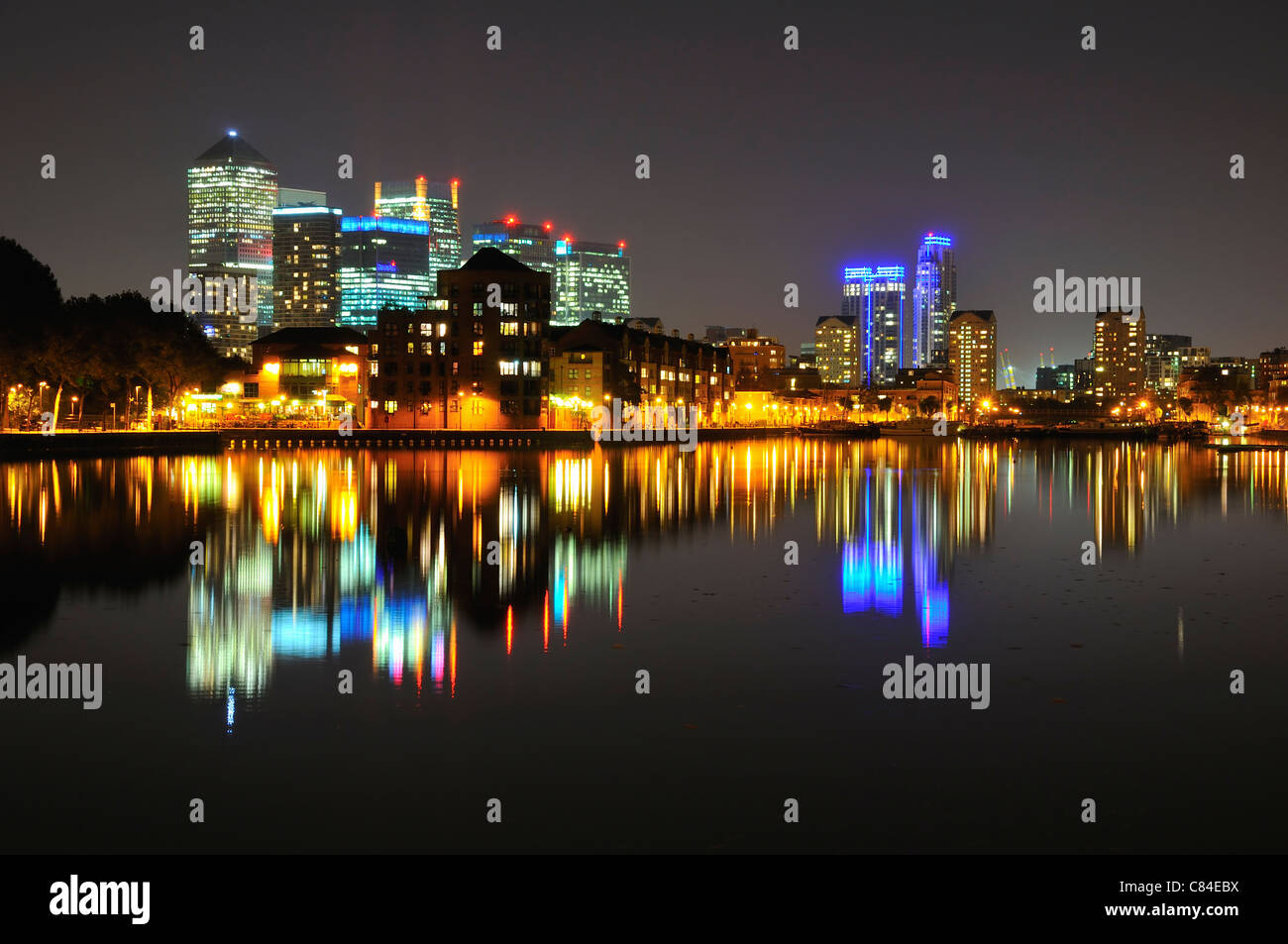 London Docklands skyline notturno, guardando verso Canary Wharf da Surrey Quays, con riflessioni in acqua Foto Stock