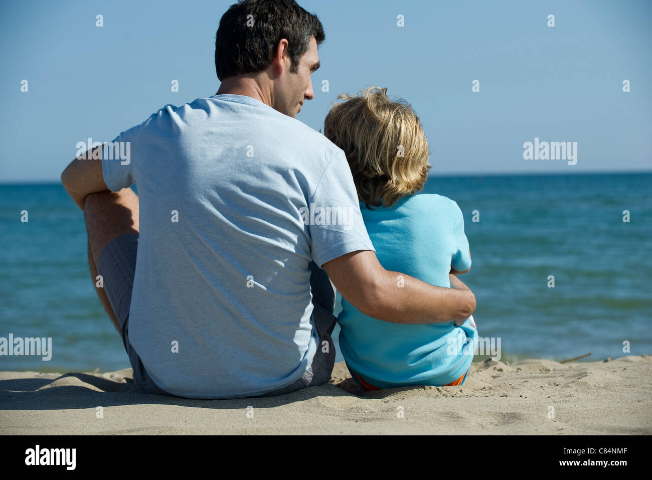 Padre e figlio seduti insieme in spiaggia, vista posteriore Foto Stock