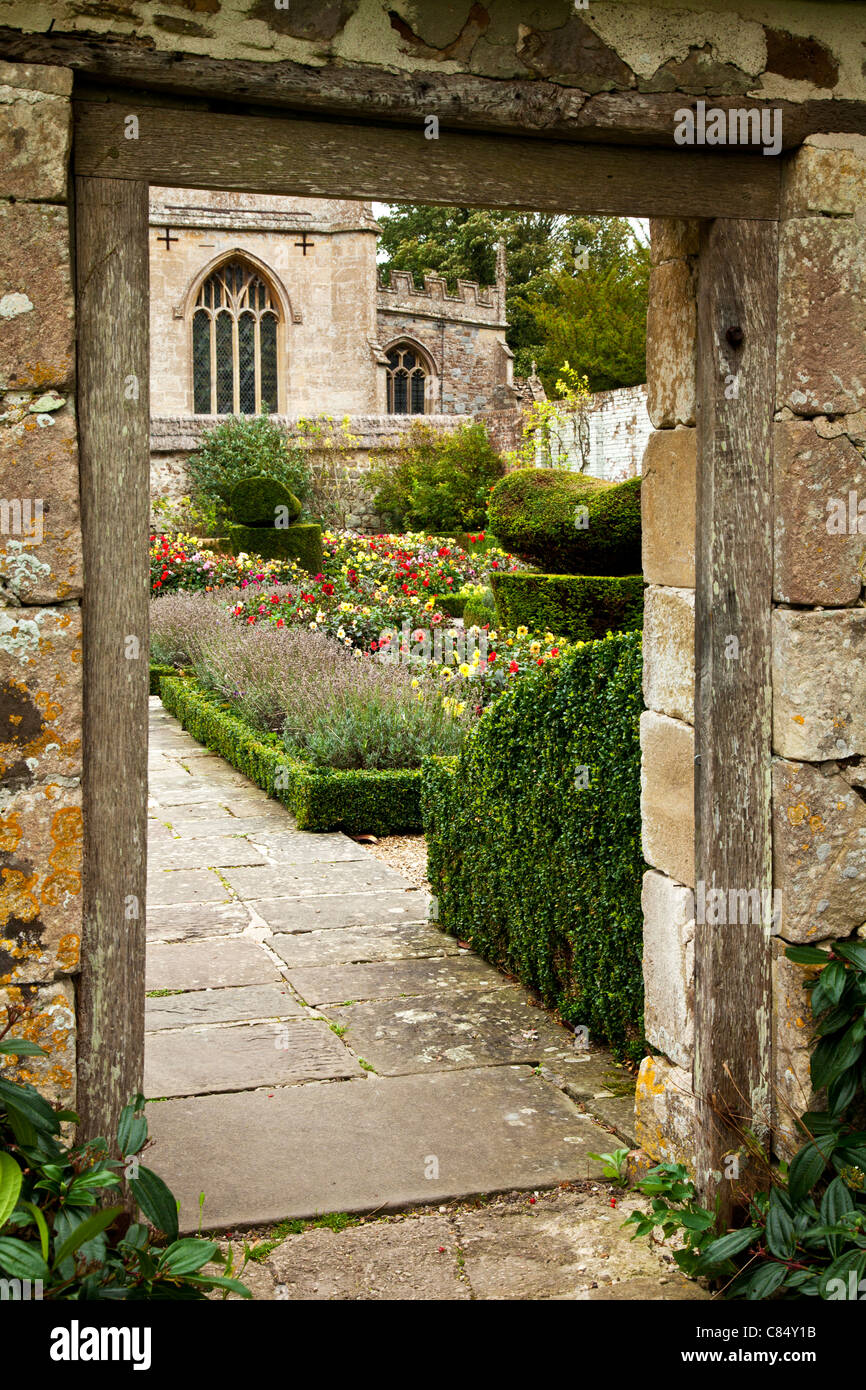 Vista attraverso una parete del giardino per un giardino formale e chiesa oltre ad Avebury nel Wiltshire, Inghilterra, Regno Unito Foto Stock
