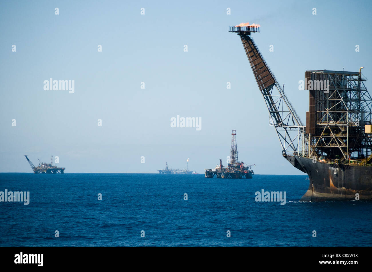 Vista di un impianto di trivellazione petrolifera campo con l'utilizzo di una FPSO sul primo piano. Campos Basin, offshore stato di Rio de Janeiro, costa del Brasile. Foto Stock