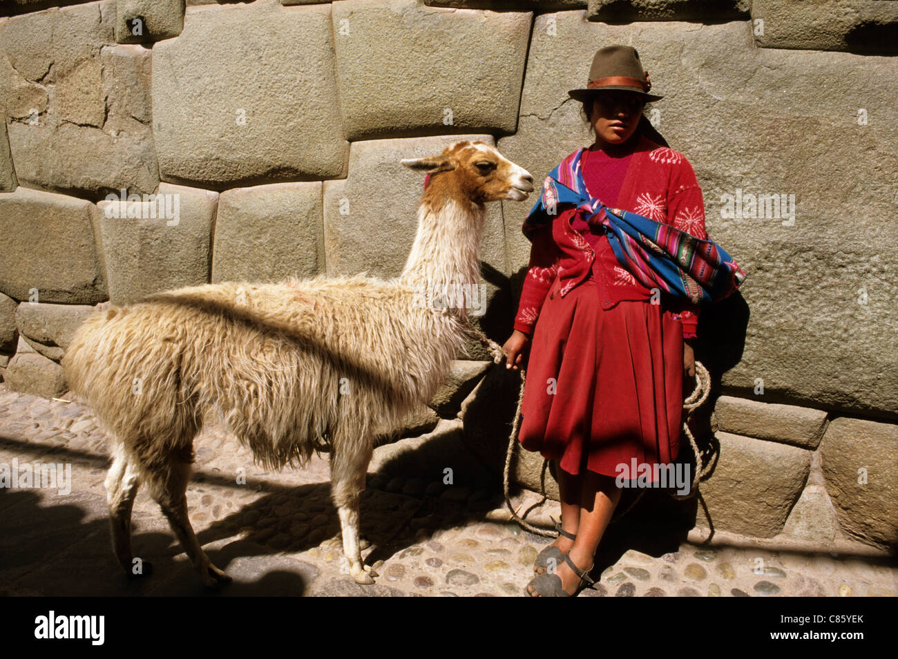 Cusco, Perù. Donna in abito tradizionale con un llama in Hatunrumiyoc dal famoso dodici facciate in pietra. Foto Stock