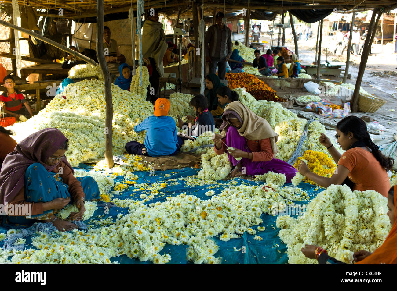 Le donne indiane e bambini al lavoro stringing ghirlande a Mehrauli Flower Market, New Delhi, India Foto Stock