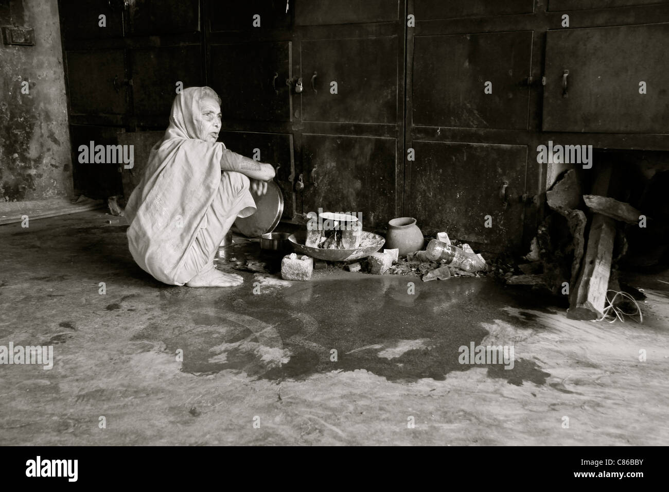 Donna senzatetto di cottura degli alimenti su una rudimentale stufa in un edificio abbandonato, Varanasi, India Foto Stock